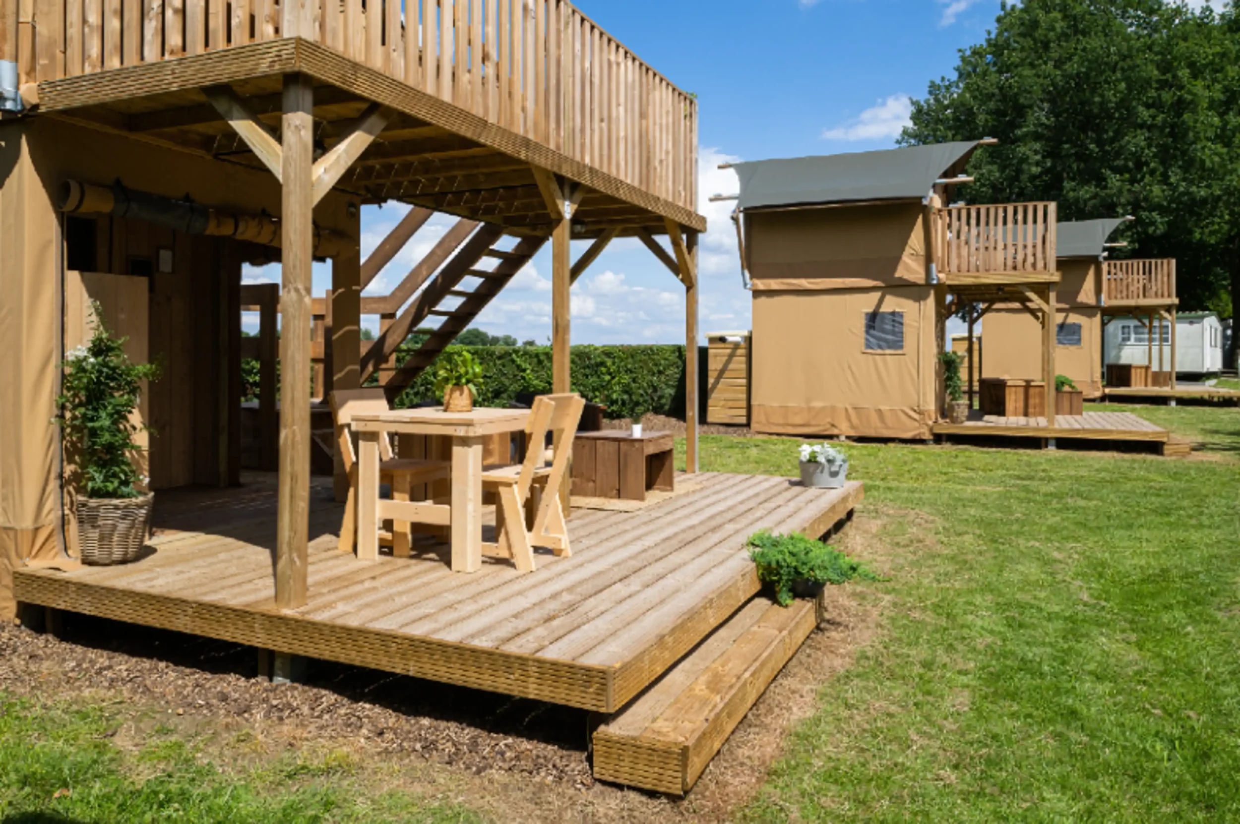 Outdoor glamping tents with wooden decks and furniture on a grassy field under a blue sky.