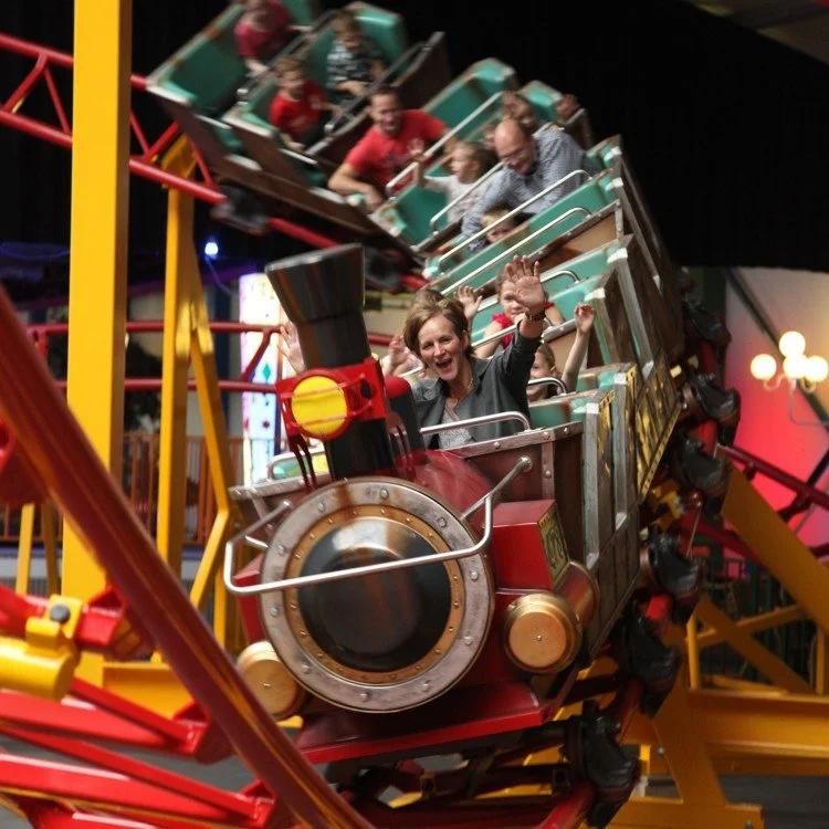 People riding on a roller coaster amusement park ride, smiling and waving.