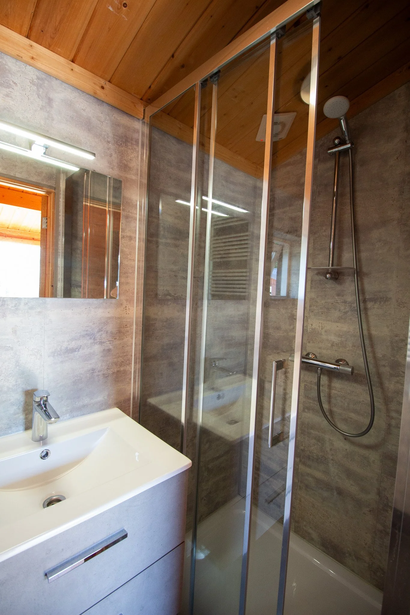 Modern bathroom with a vanity sink, mirror, and a glass-enclosed shower with a wooden ceiling.