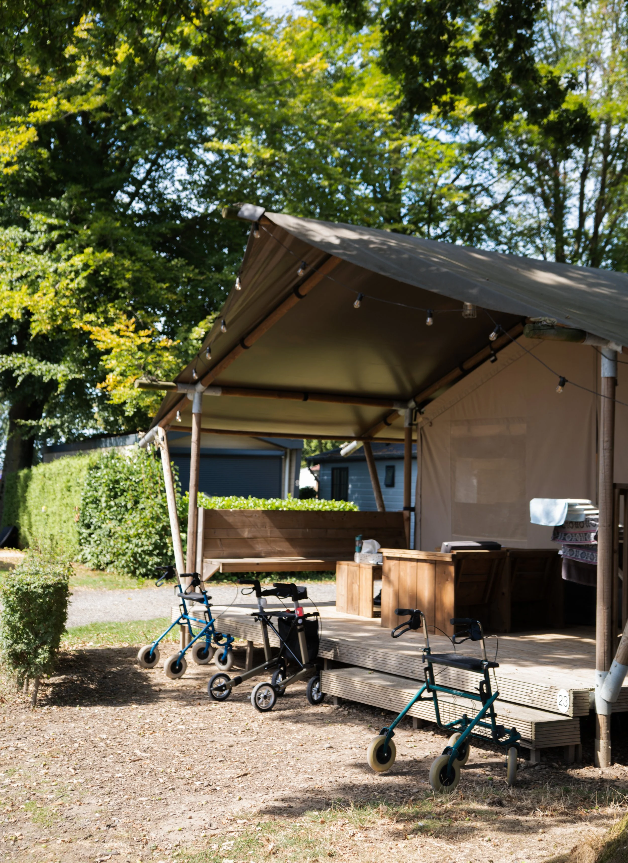 Outdoor porch area with four mobility scooters parked, surrounded by green trees and bushes, with a shed visible in the background.