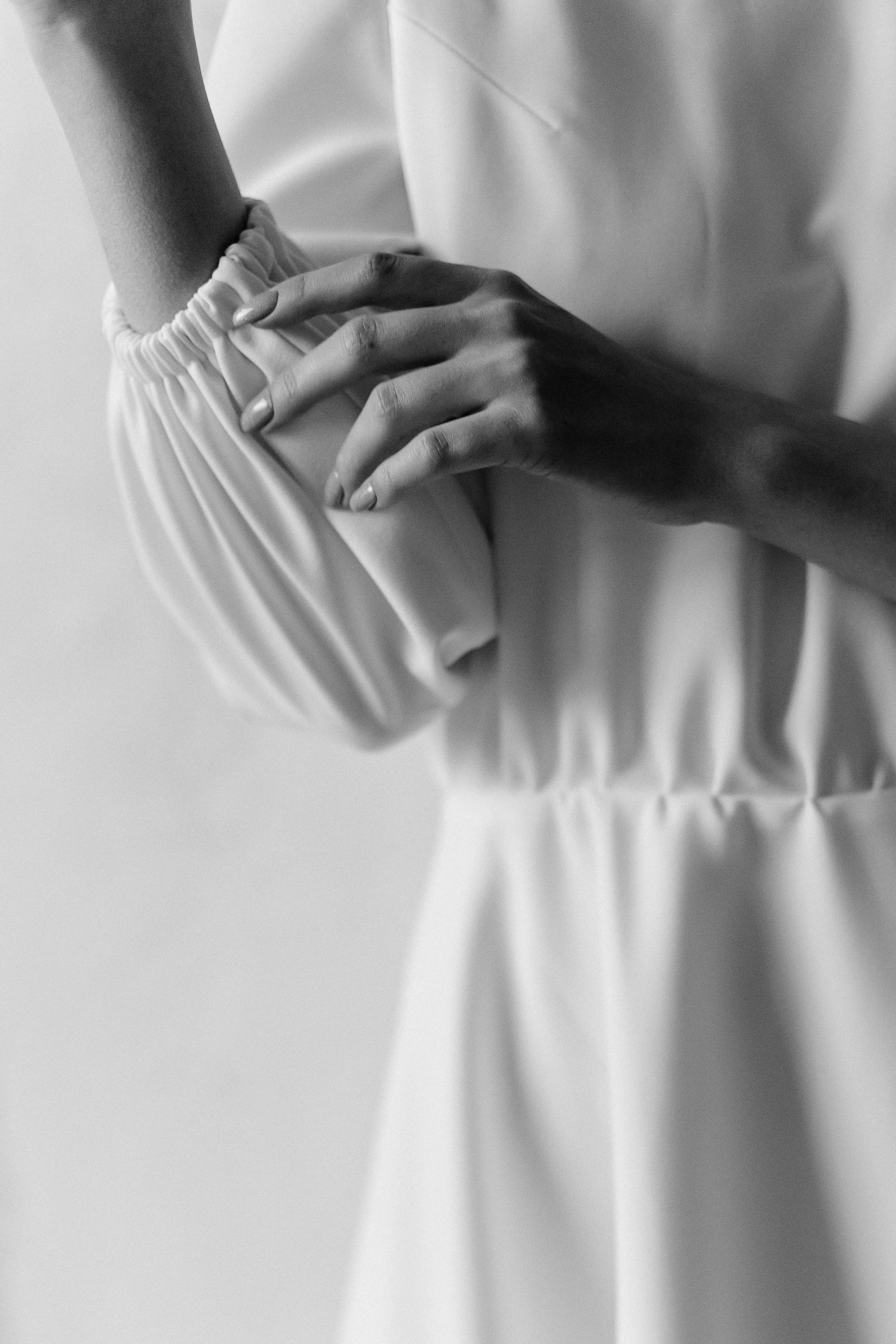 A person wearing a light-colored garment adjusts the elastic waistband of their pants with their hand.