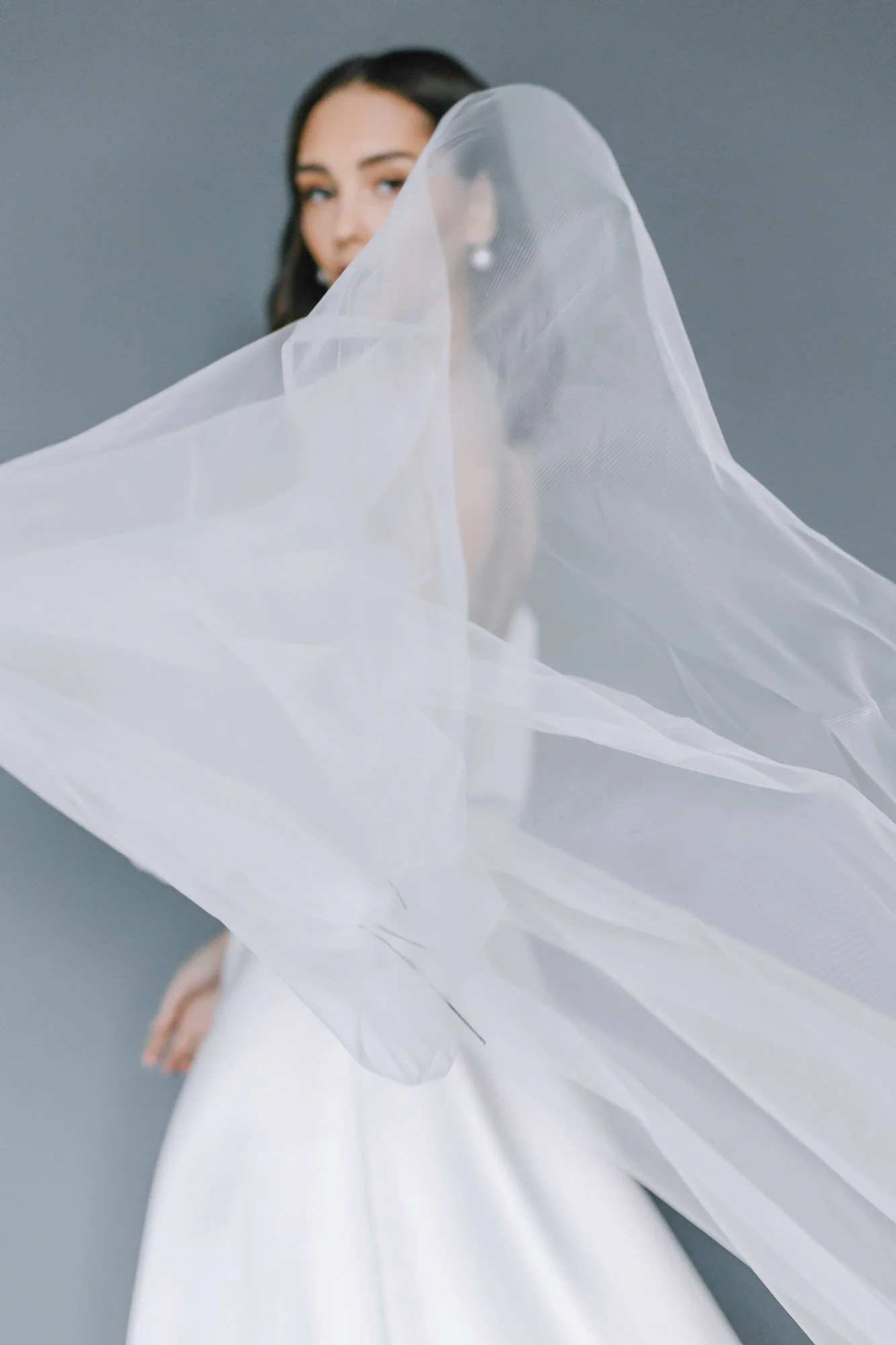 A woman with dark hair and blue eyes wearing a white dress and a sheer veil.