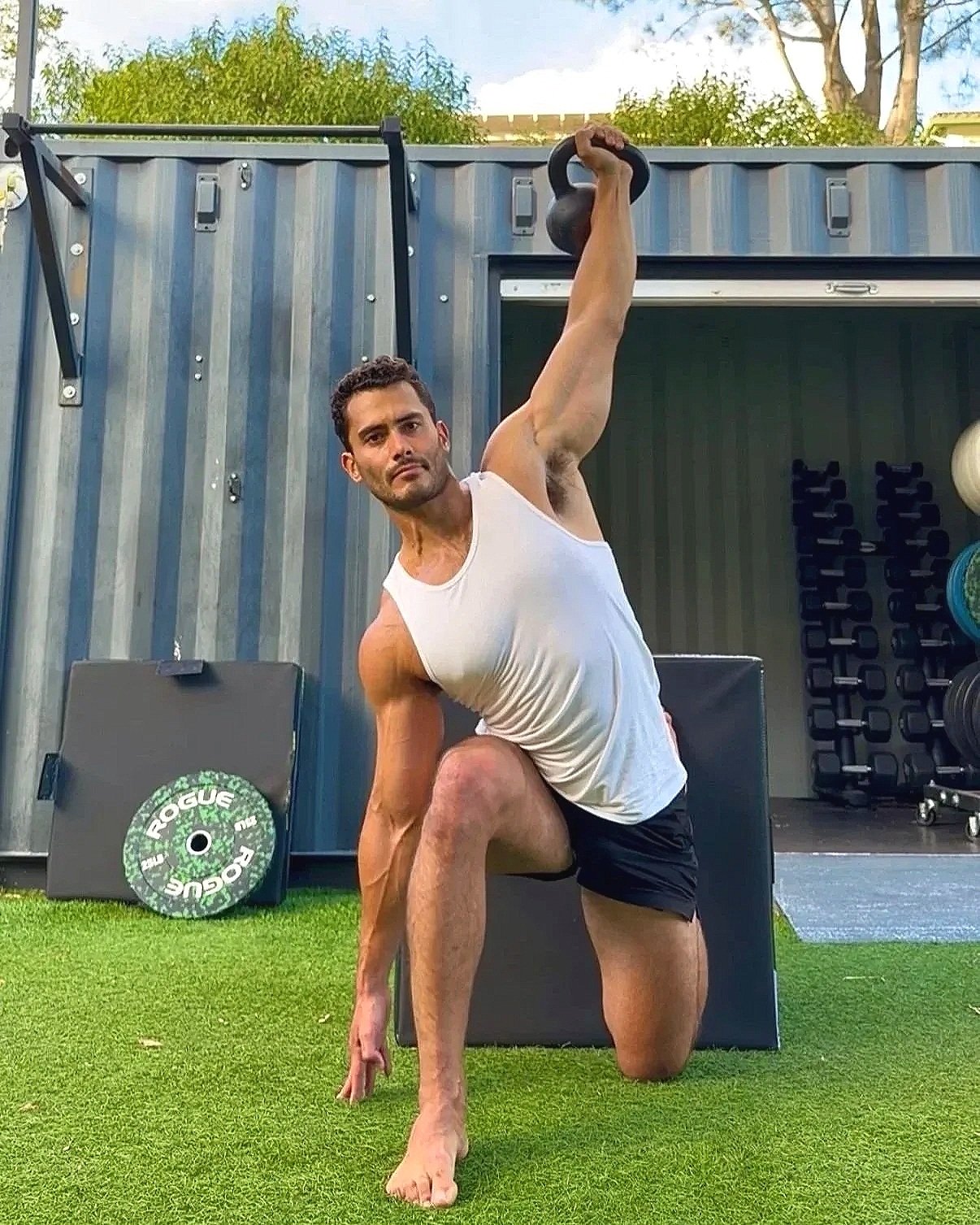 Man performing a yoga pose with a kettlebell outdoors at a gym.