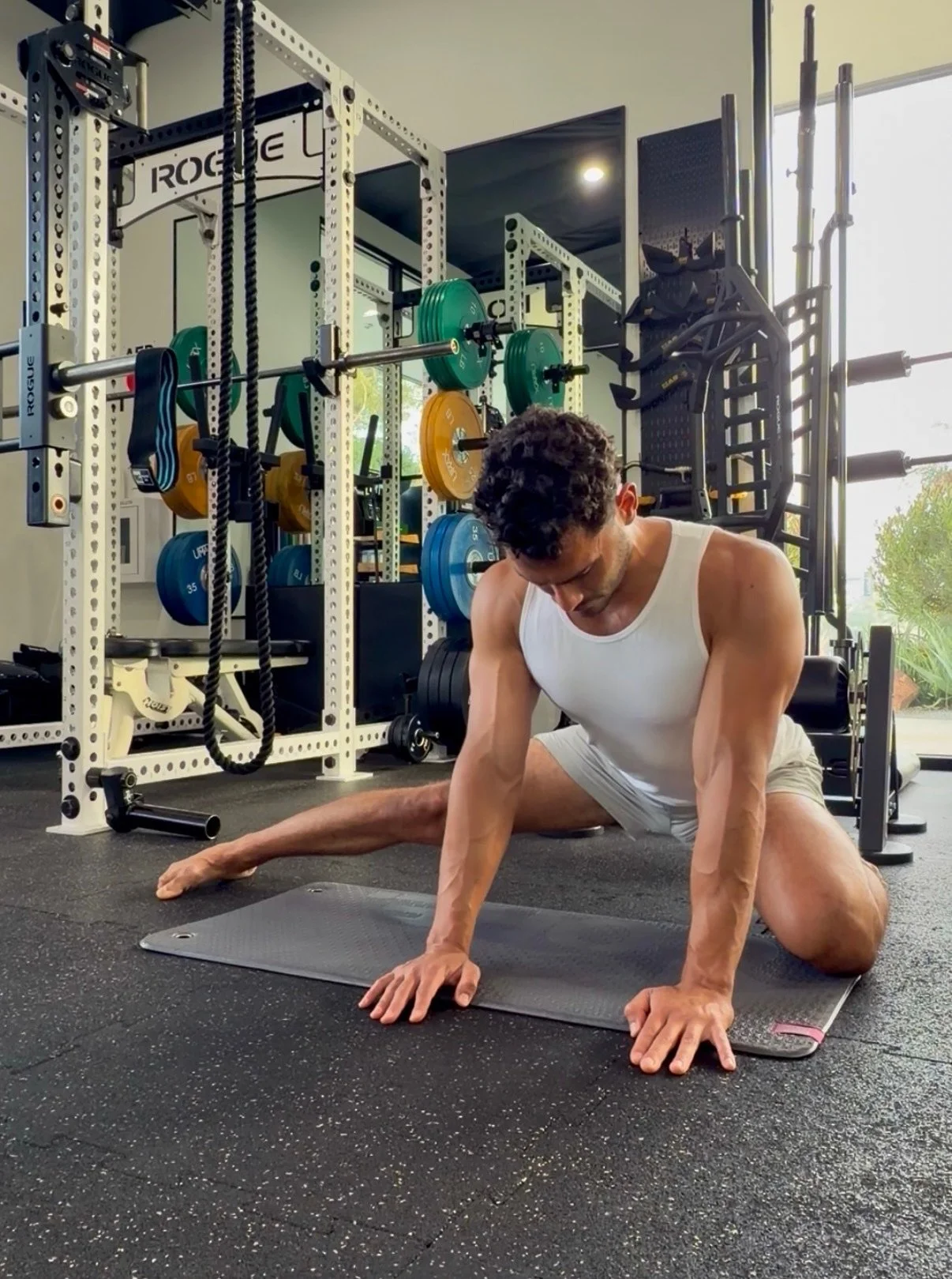 Man stretching on a yoga mat in a gym, surrounded by weightlifting equipment and colorful weights.