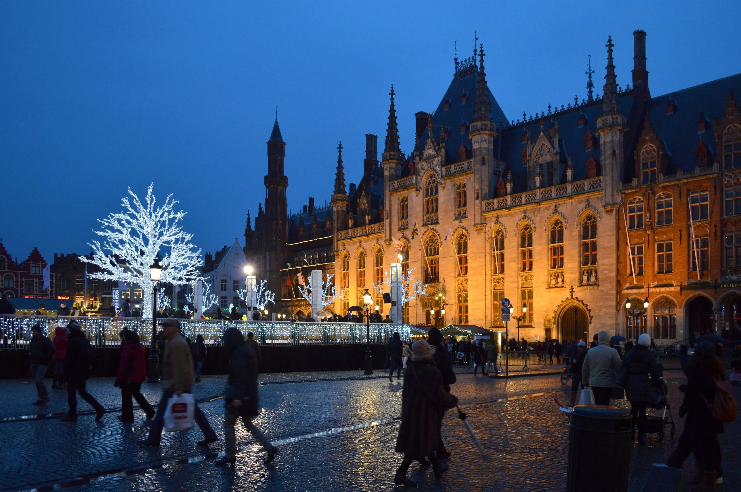 Christmas market lights illuminating historic buildings and cobblestone streets in Bruges, Belgium.
