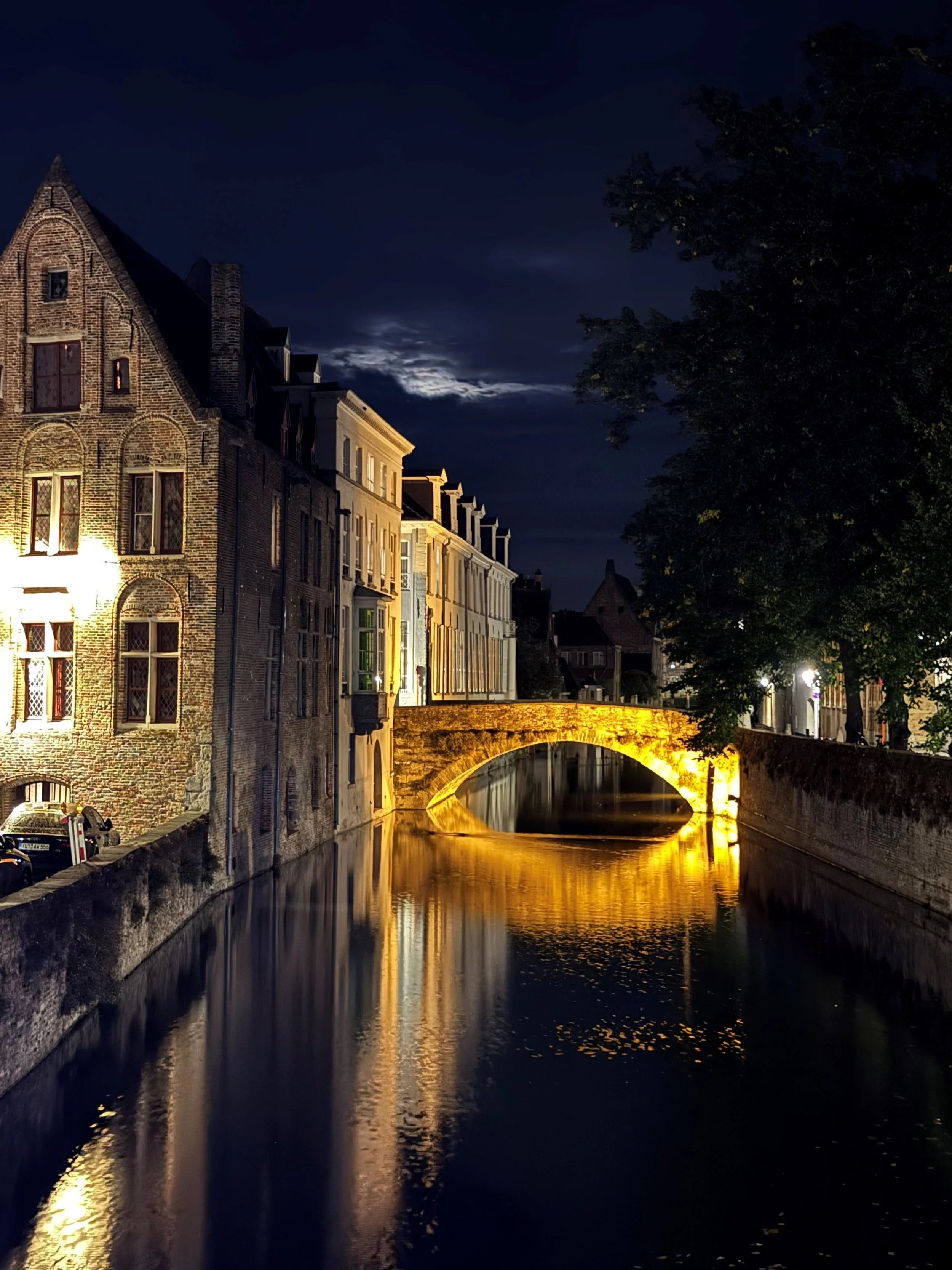 Illuminated stone bridge over a canal in Bruges at night, surrounded by historic buildings.