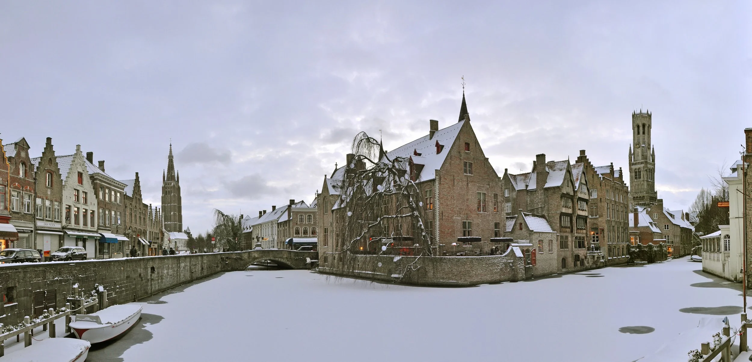 Winter evening at Rozenhoedkaai in Bruges, Belgium, with illuminated medieval buildings reflected in the canal.
