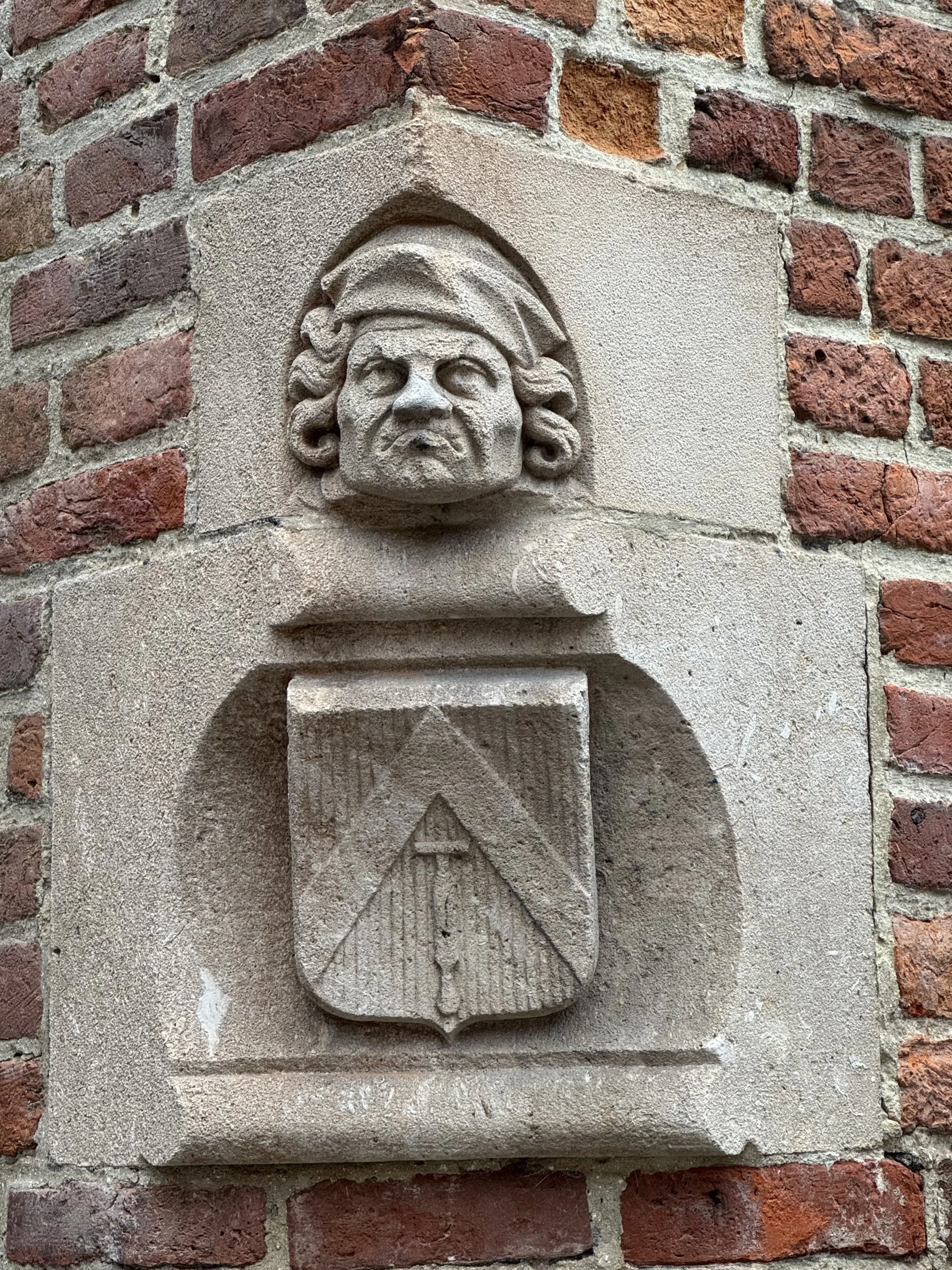 Small carved stone face on a brick wall in Huidenvettersplein, Bruges.