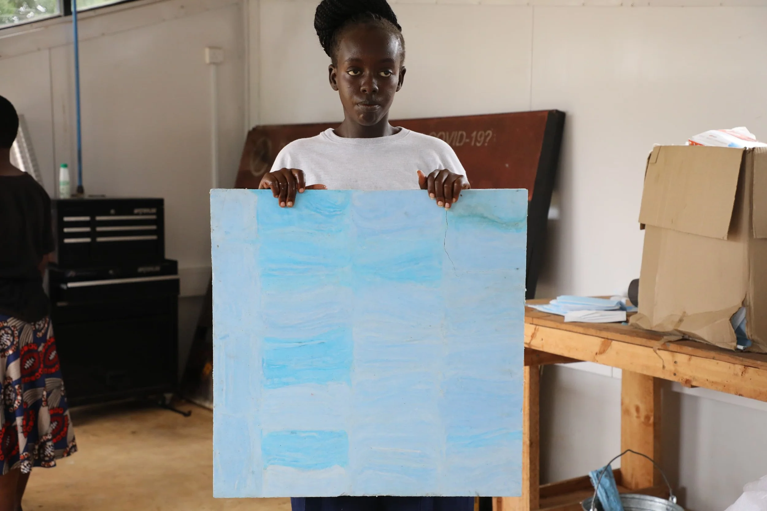 Young woman in a fab lab in kenya holding a sheet made with face masks, made using the mad plastic sheet press 
