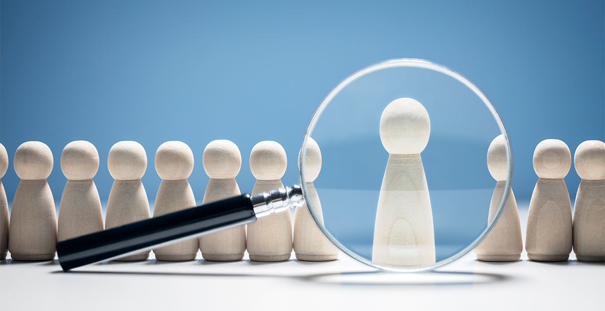 A row of wooden game pawns with a magnifying glass focused on a single pawn, highlighting it in the center against a blue background.