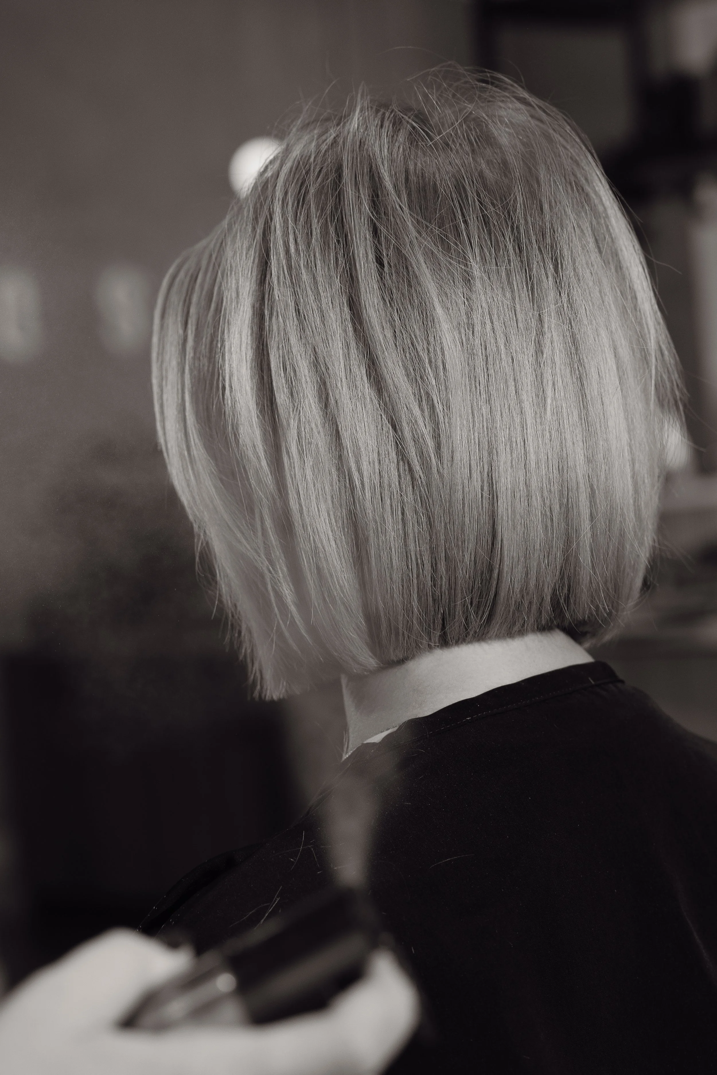 A person with shoulder-length gray hair, viewed from behind, in a black and white photo.