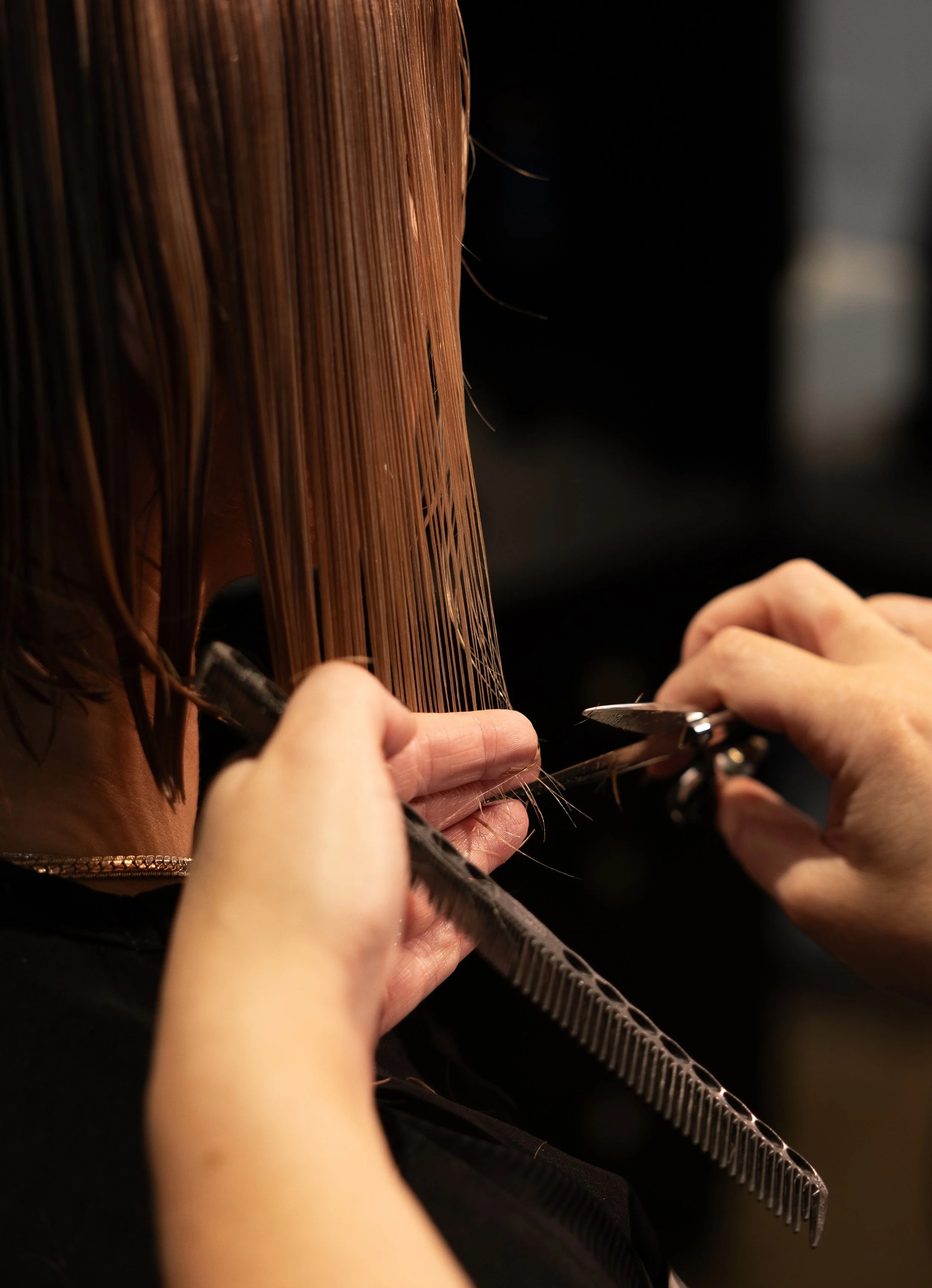 A hairstylist cuts a woman's hair with scissors while using a comb to section the hair.