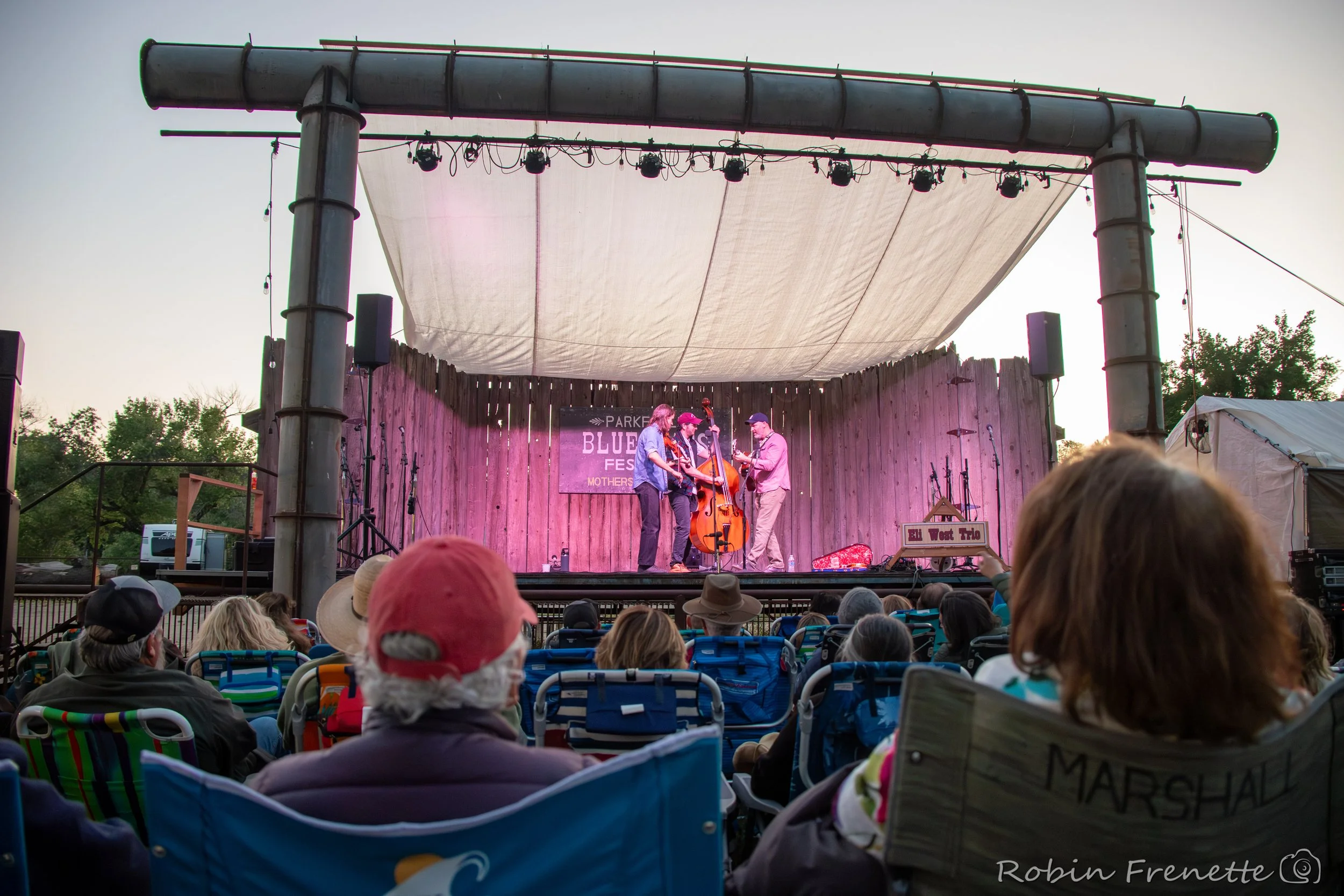 People sitting in chairs watching a live music at the Parkfield Bluegrass Festival main stage.
