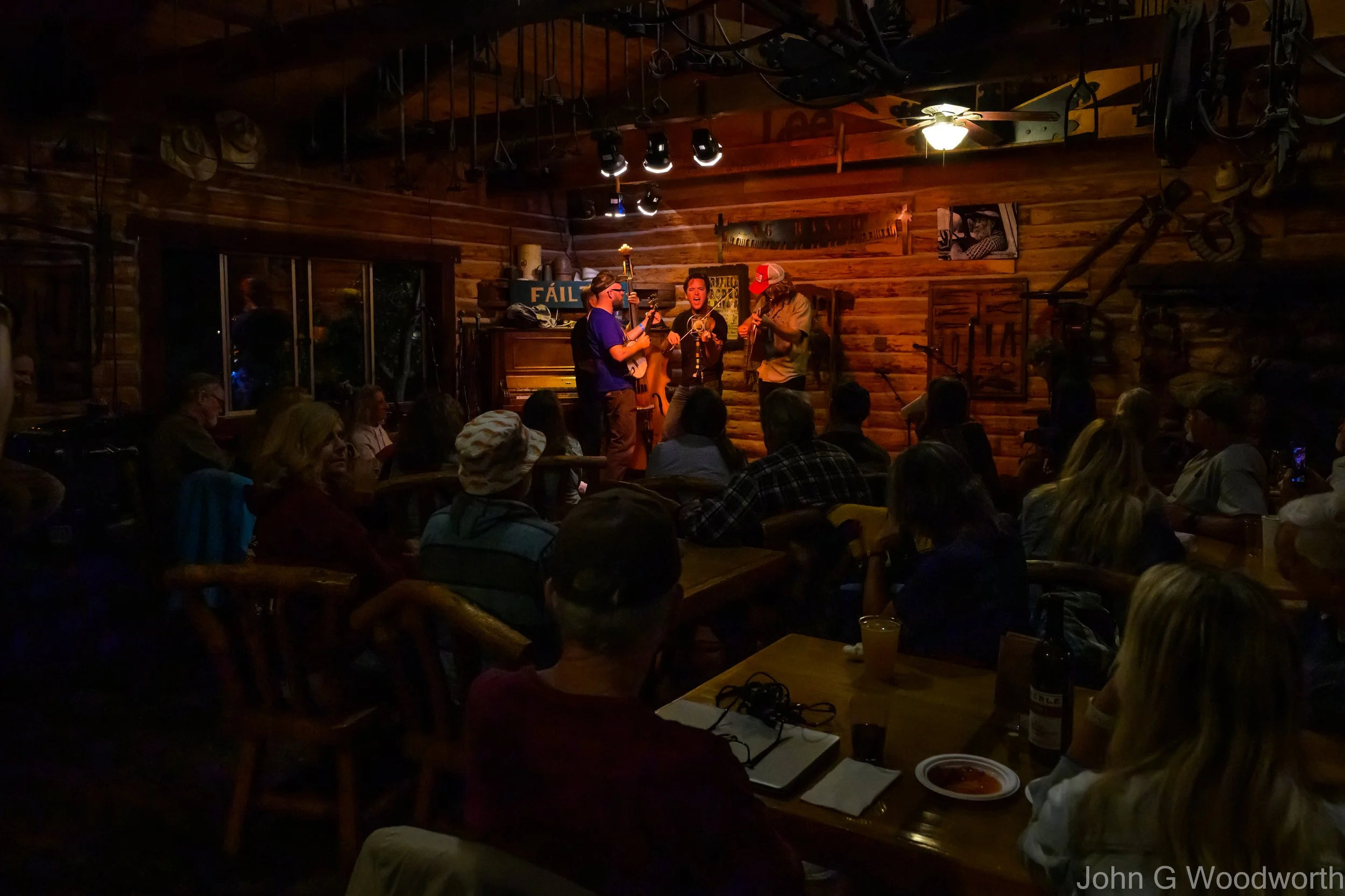 A live music performance in the Parkfield Cafe at the Parkfield Bluegrass Festival with three musicians on stage and the audience seated at tables enjoying the show.