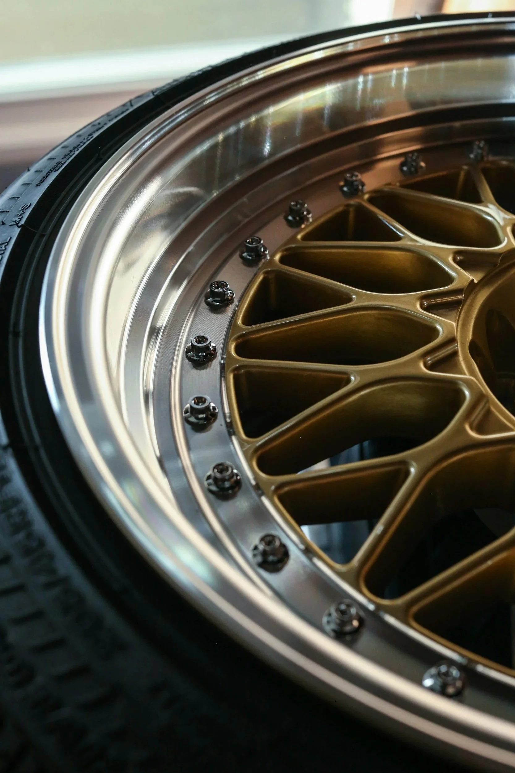 Close-up of a gold-colored car wheel rim with a black tire, featuring multiple small bolts around the rim.