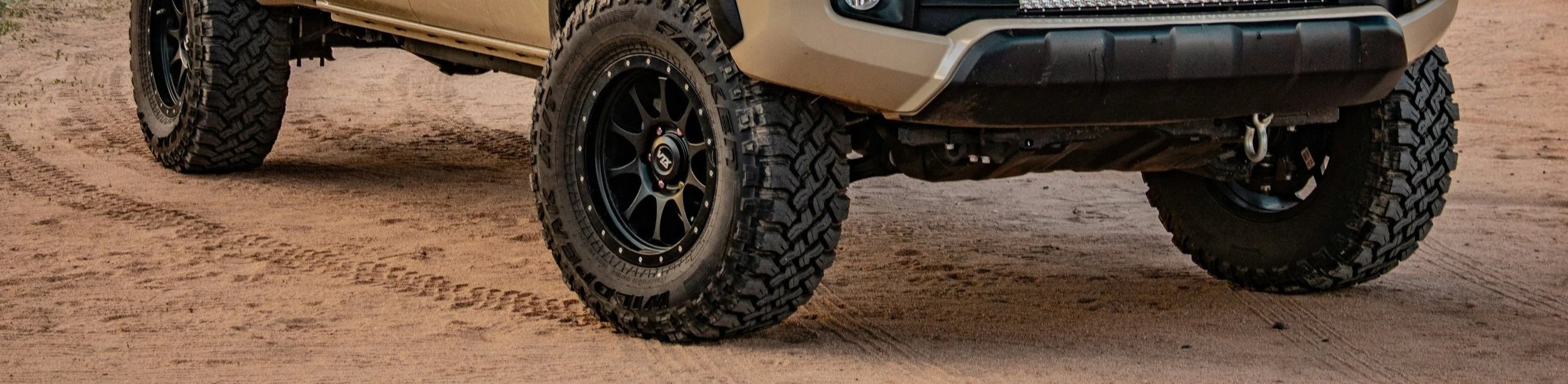 Close-up of the front and rear tires of an off-road vehicle on a dirt surface, showcasing rugged tread patterns and black rims.