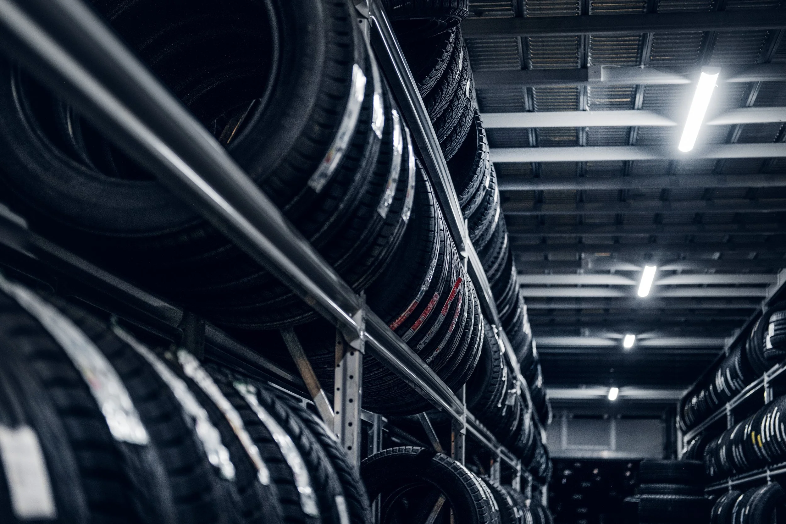 A warehouse with shelves filled with stacked tires under fluorescent lighting.