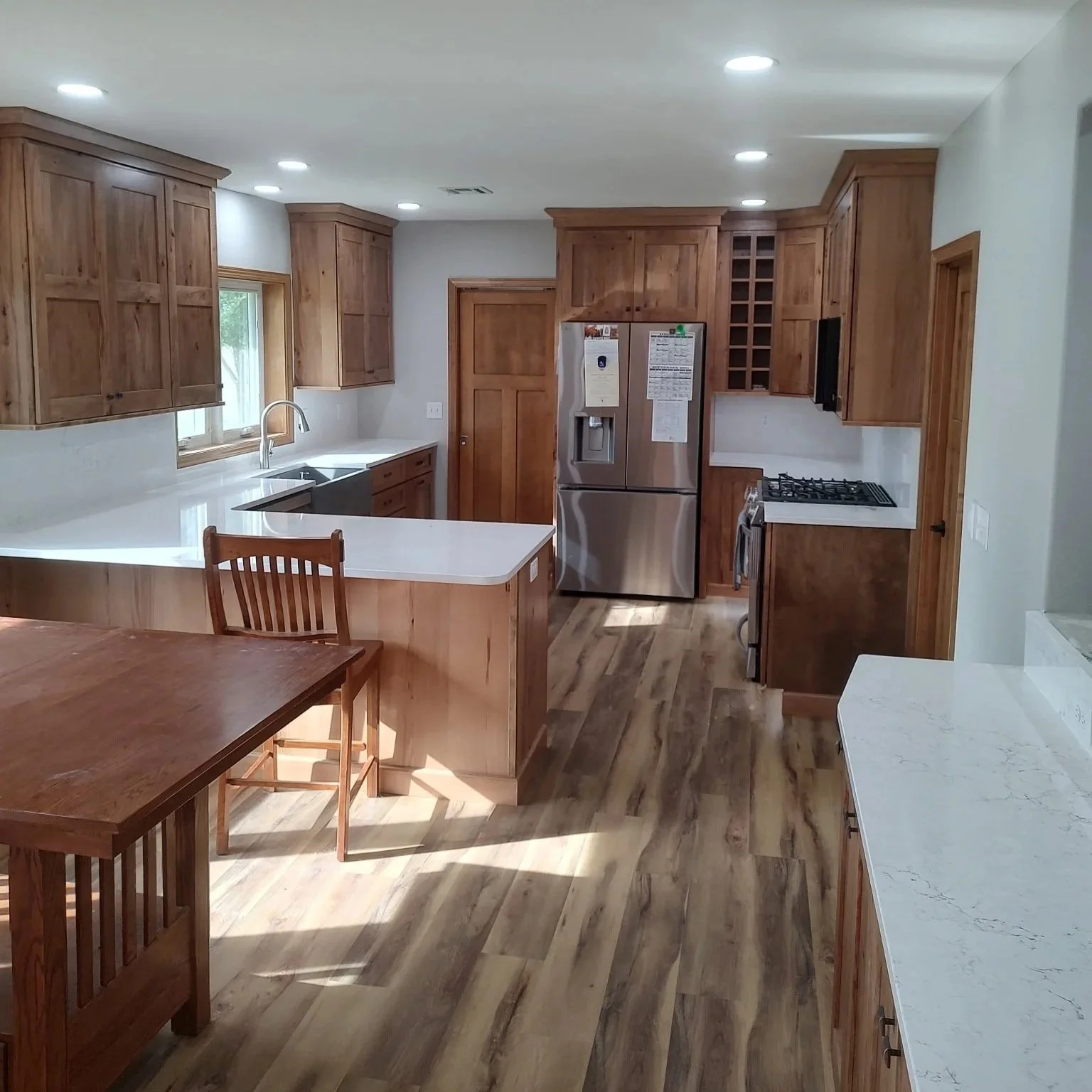 Kitchen with wooden cabinets, white countertops, stainless steel refrigerator, gas stove, wooden dining table, and wood flooring.