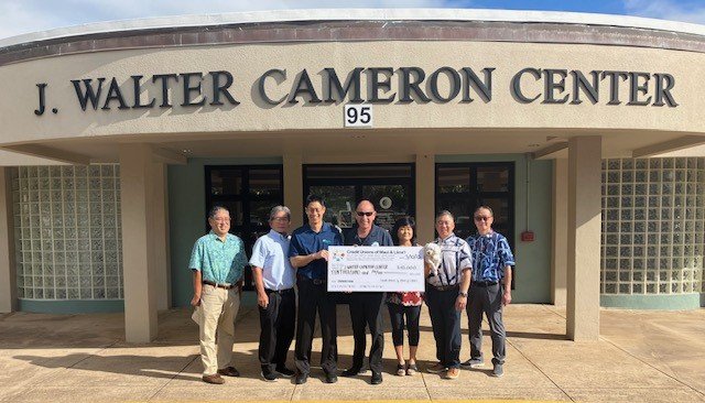 Group of seven people standing outside the J. Walter Cameron Center, holding a large check.