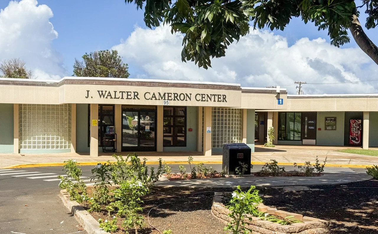 Front view of J. Walter Cameron Center building with clear sky, trees, plants, and vending machine outside.
