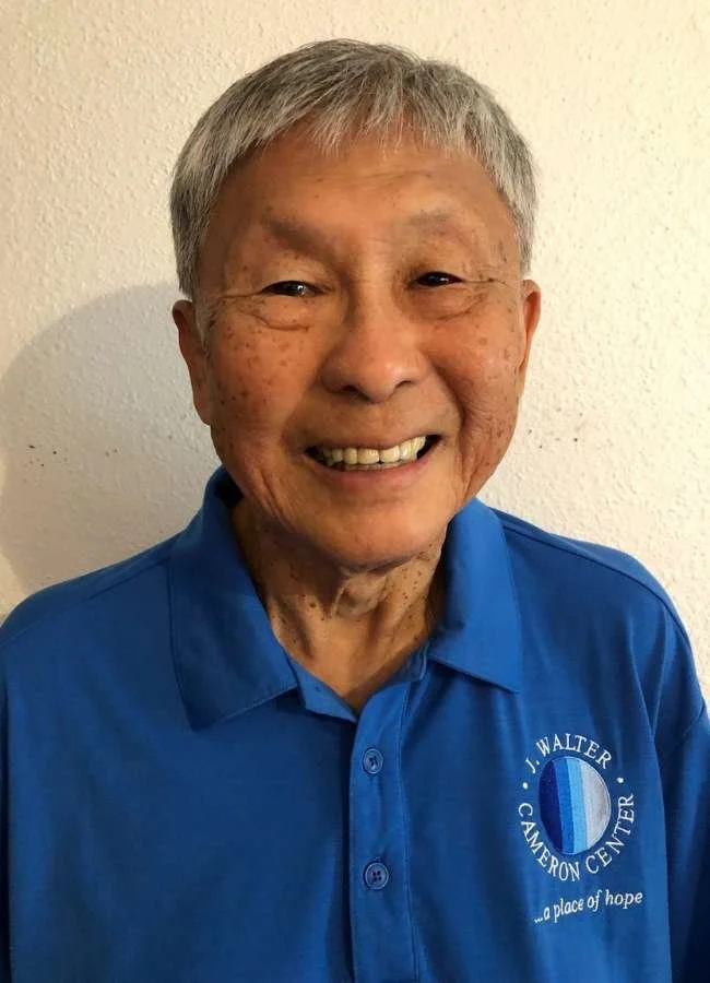 Smiling elderly man with gray hair wearing a blue polo shirt with a logo for I. Walter Cameron Center.