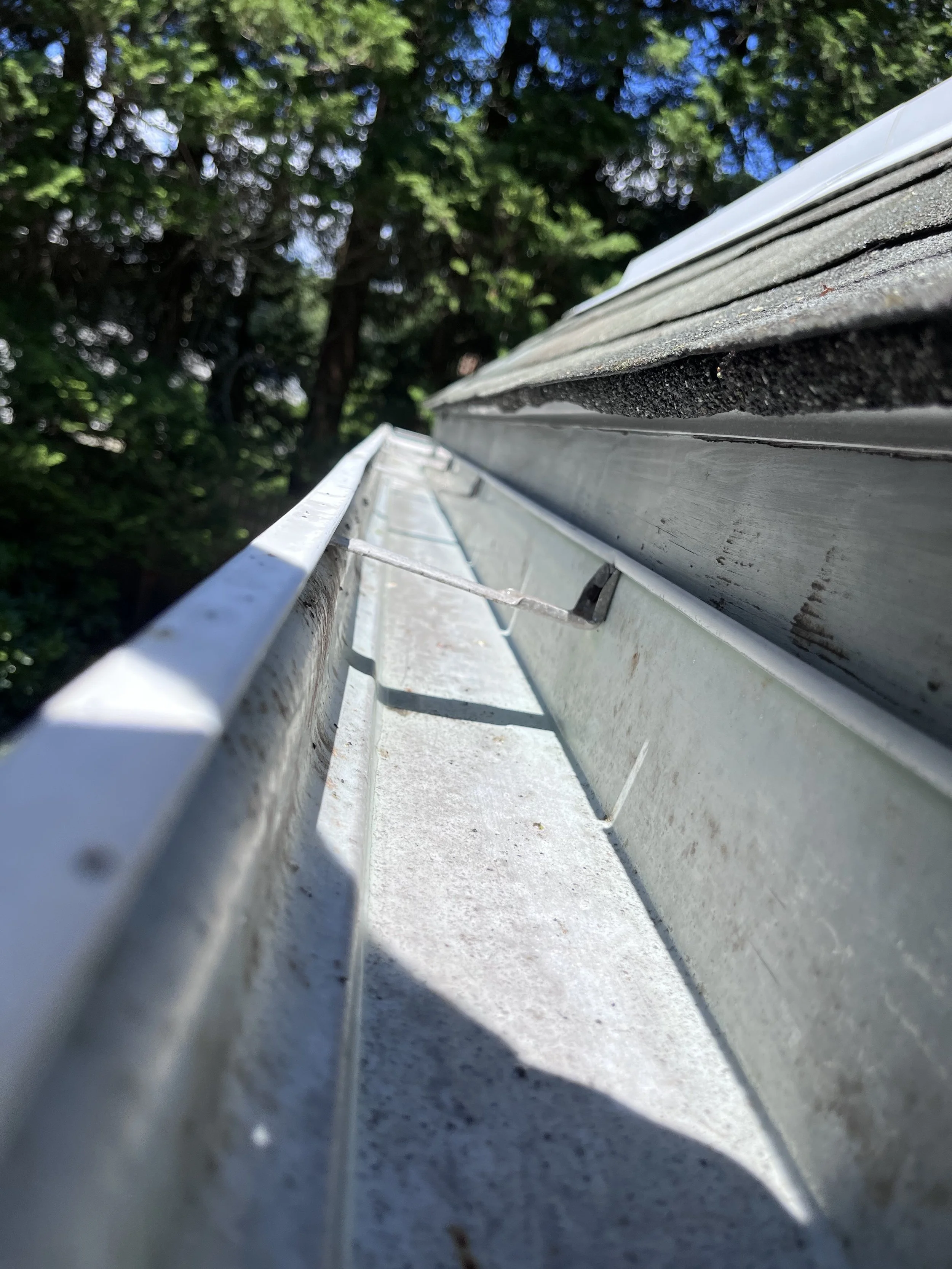 Close-up view of a house's cleaned gutter system from below, with trees in the background.