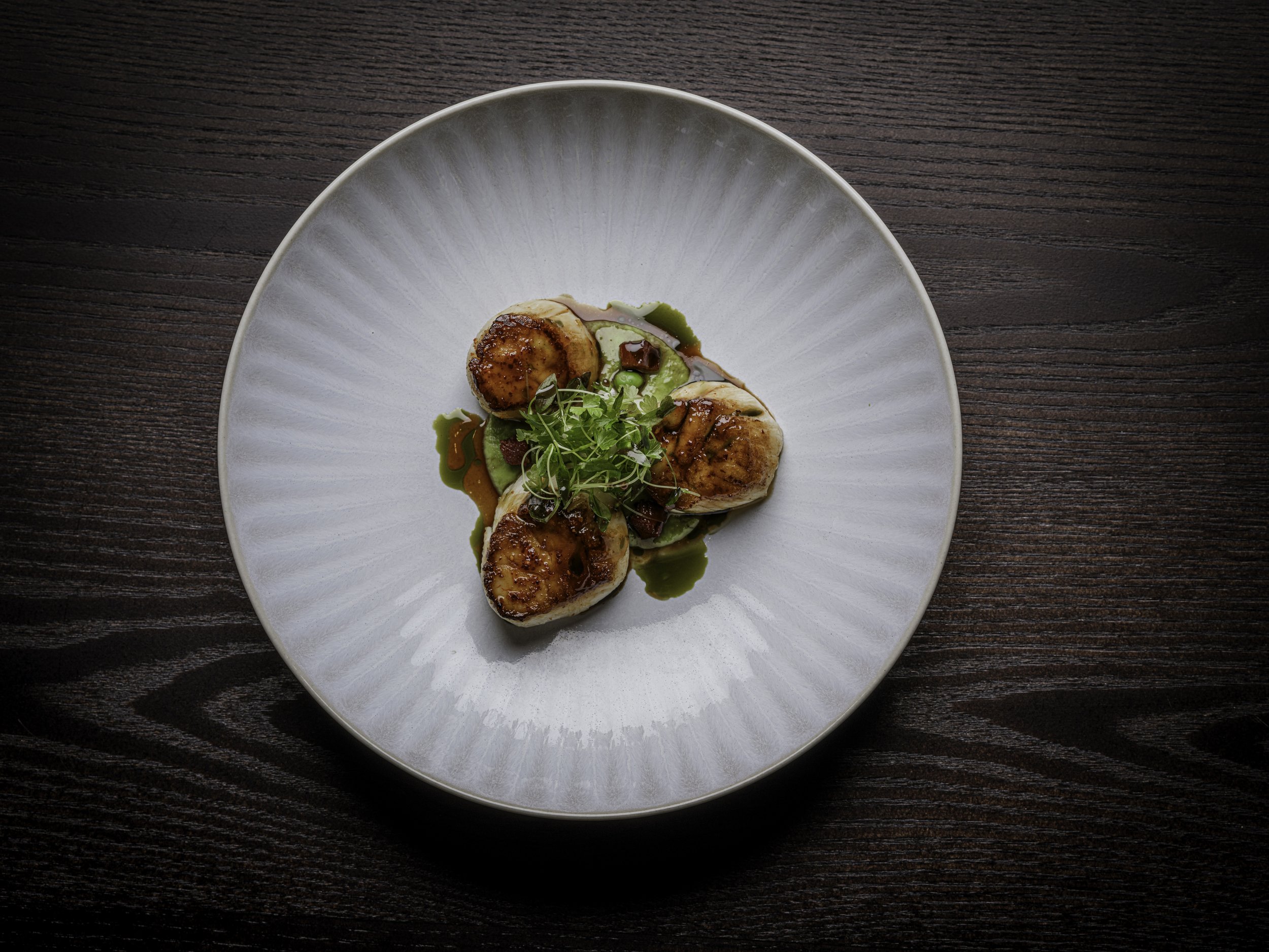 A plate of scallops with sauce and greenery