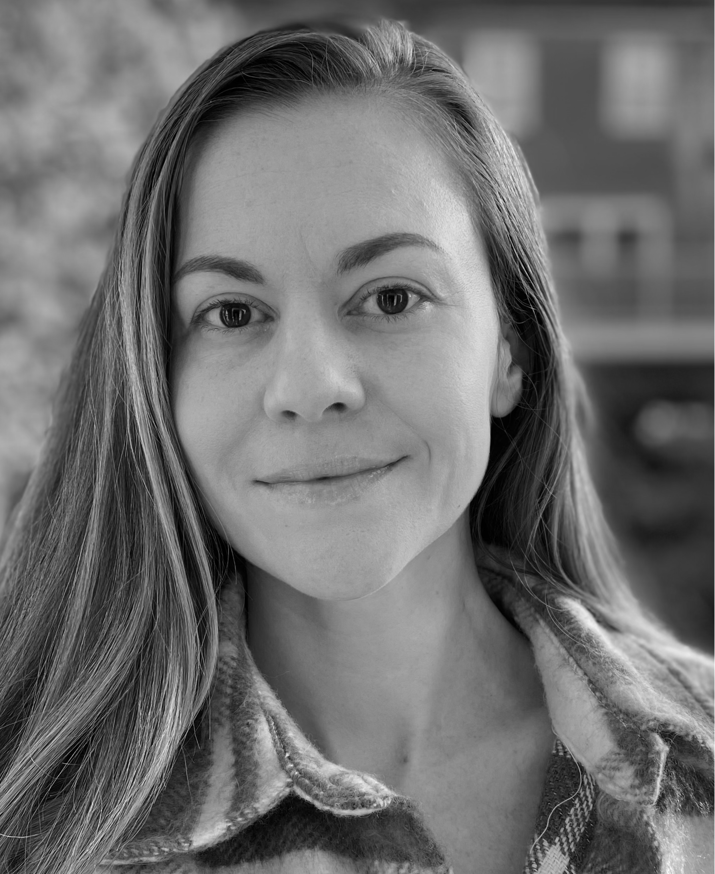 Close-up black and white photo of a woman with long hair, smiling slightly, wearing a plaid shirt.