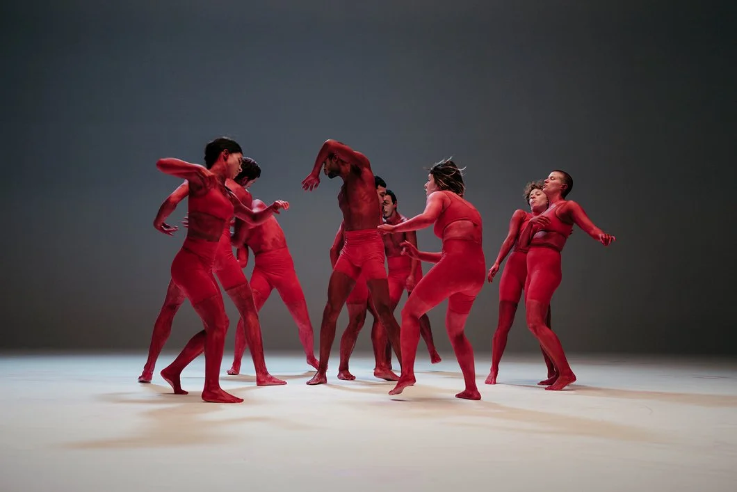 Groupe de danseurs nus peints en rouge, en mouvement sur scène