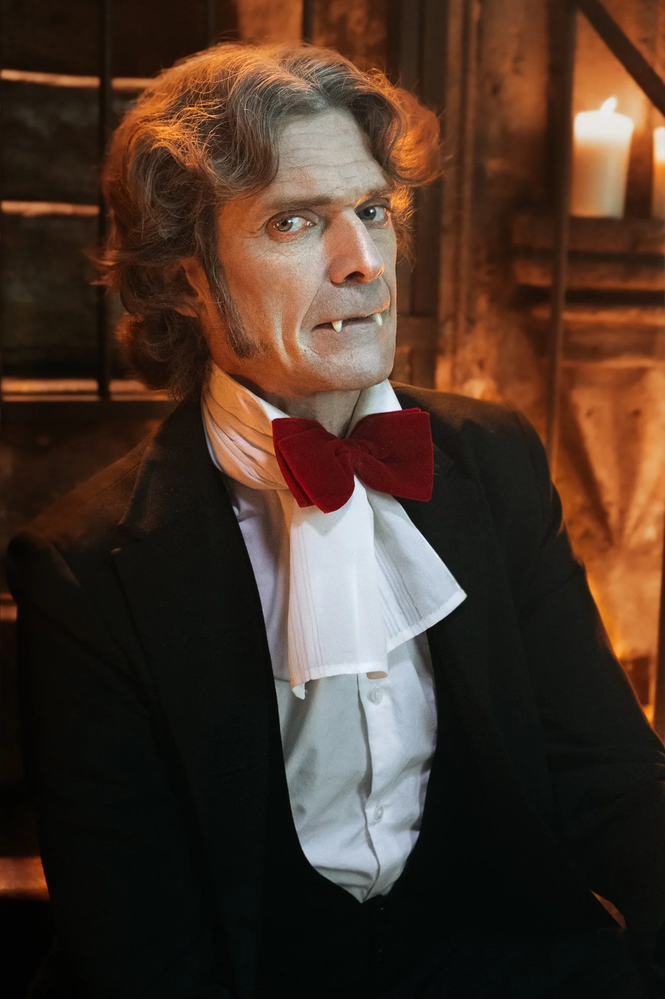 Une statue ou un mannequin représentant un homme portant un smoking noir avec un nœud papillon rouge, dans un décor en bois avec des bougies.