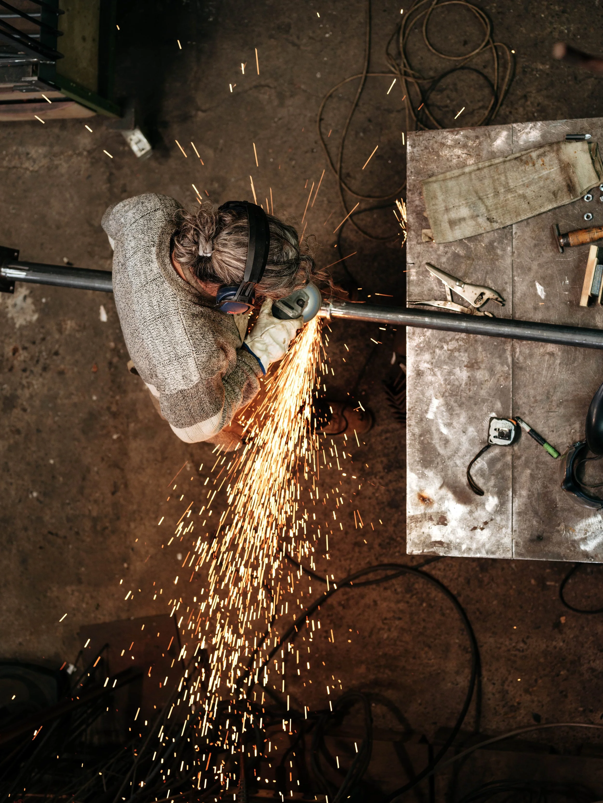 Une personne qui travaille avec une machine de soudage, produisant des étincelles, dans un atelier ou un espace de construction, portant des équipements de sécurité comme des gants et un casque