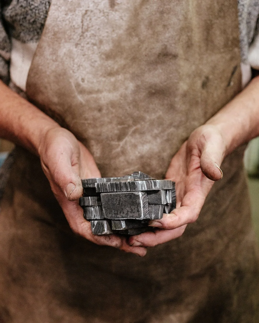 Une personne portant un tablier sale tient des pièces métalliques dans ses mains usées, indiquant qu'elle travaille dans un atelier ou une usine de fabrication ou de réparation.
