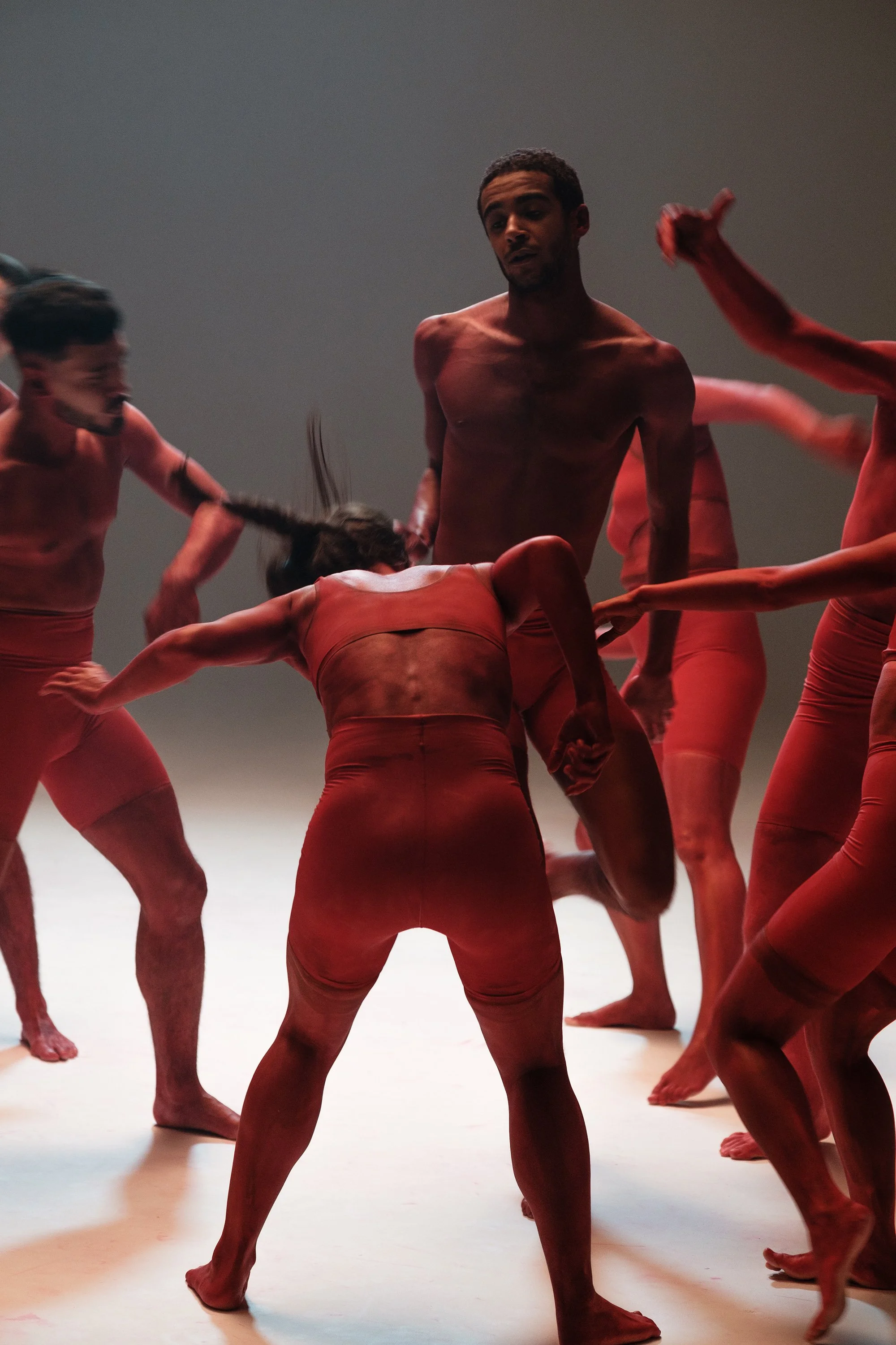 Groupe de danseurs nus avec des costumes de couleur rouge sur scène, en mouvement dynamique.
