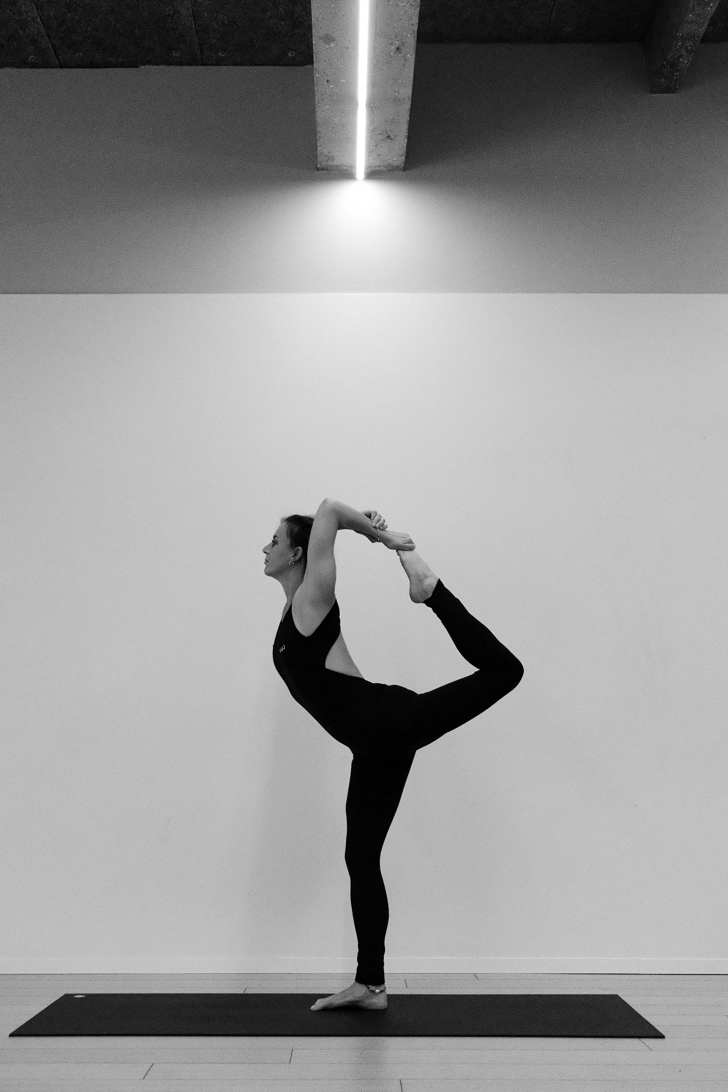 Femme en position de yoga, portant un legging noir, dans une salle minimaliste en noir et blanc.