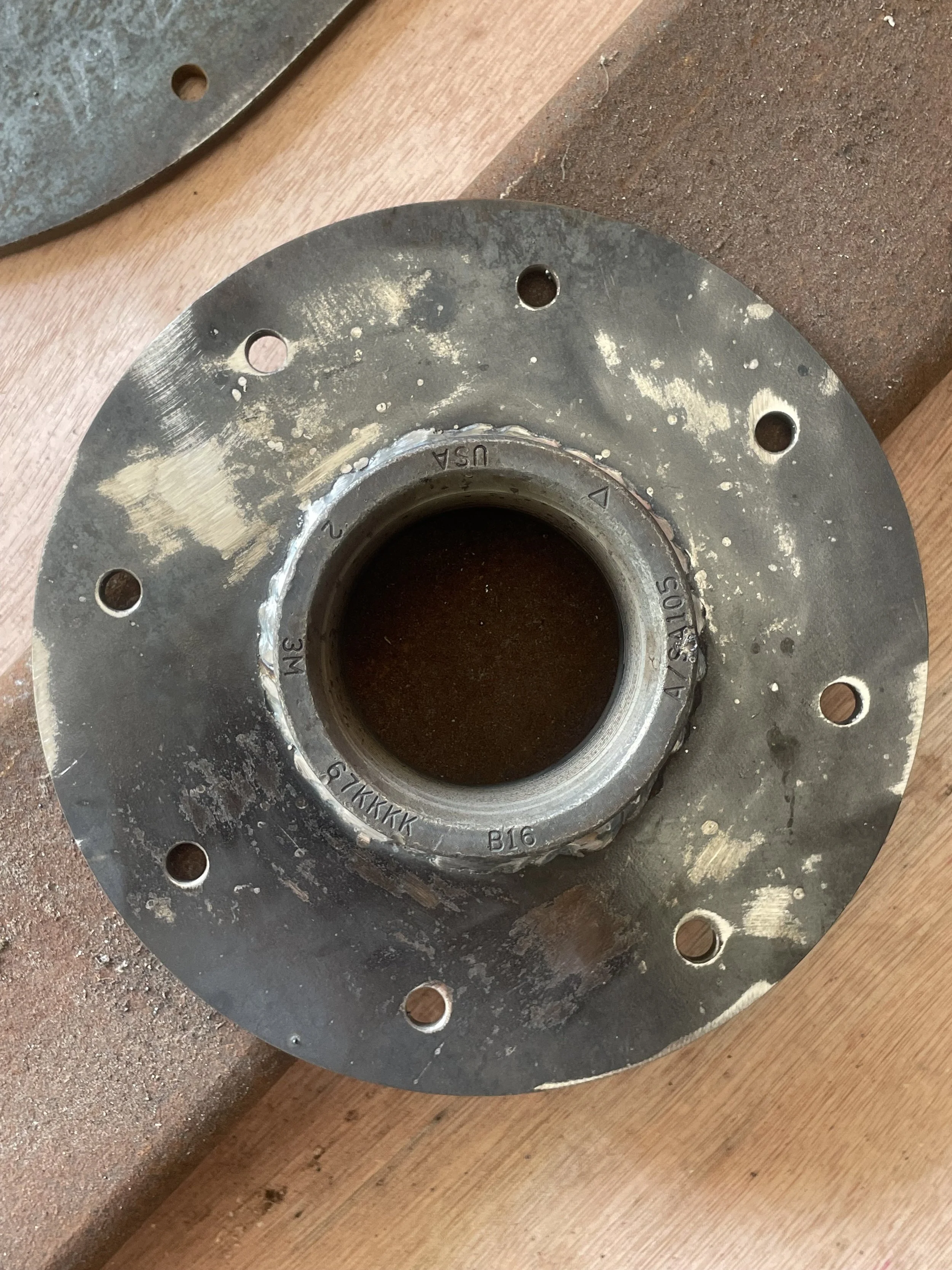 A metal wheel hub sitting on a wooden surface, with scratches and dirt on its surface.
