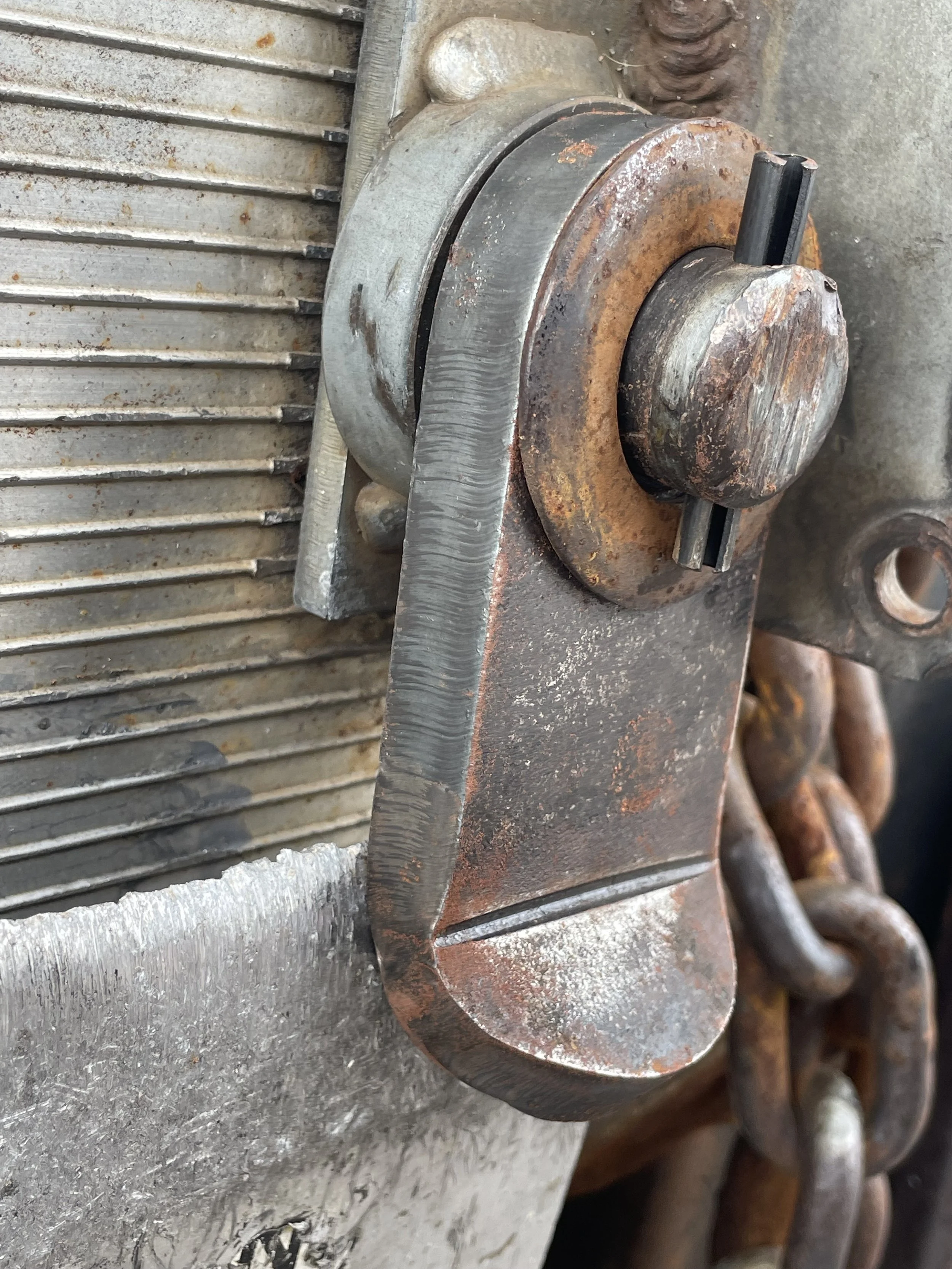 Close-up of a rusty metal chain, roller, and chain tensioner on a piece of industrial or mining equipment.