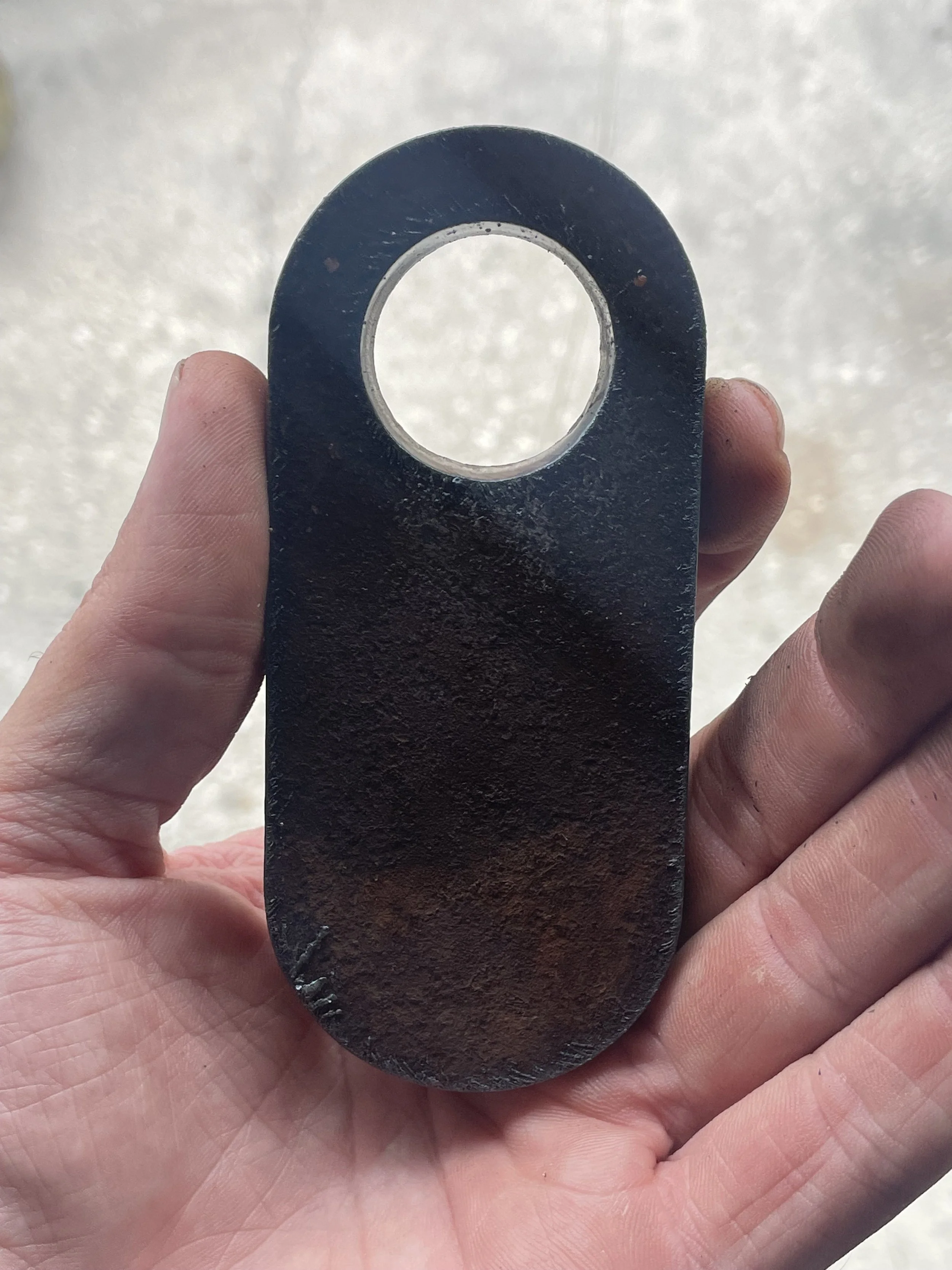 Person holding a black, oval-shaped metal object with a large circular hole at the top and a smaller hole at the bottom, against a light background.