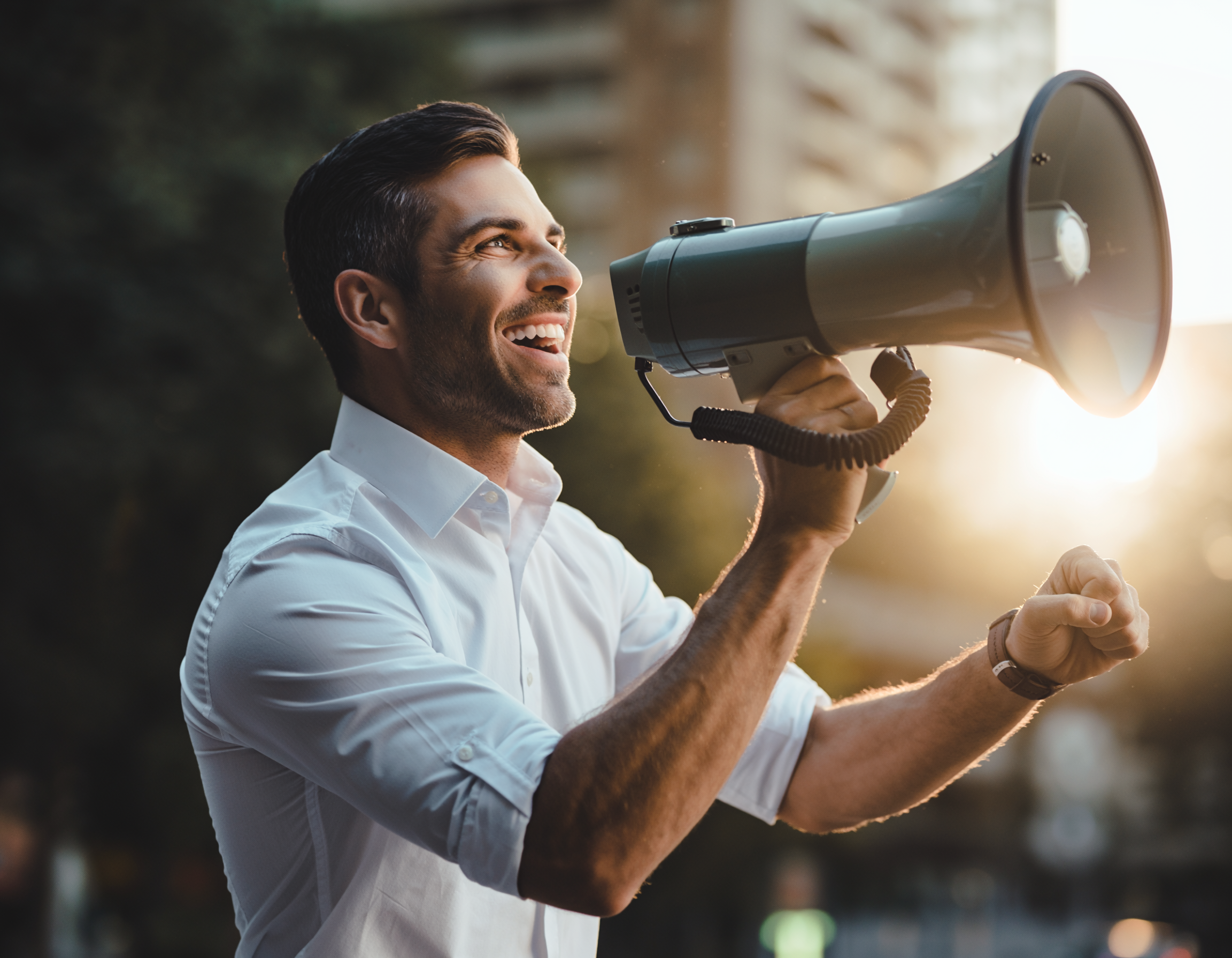 Happy man in white shirt using a megaphone outdoors at sunset.
