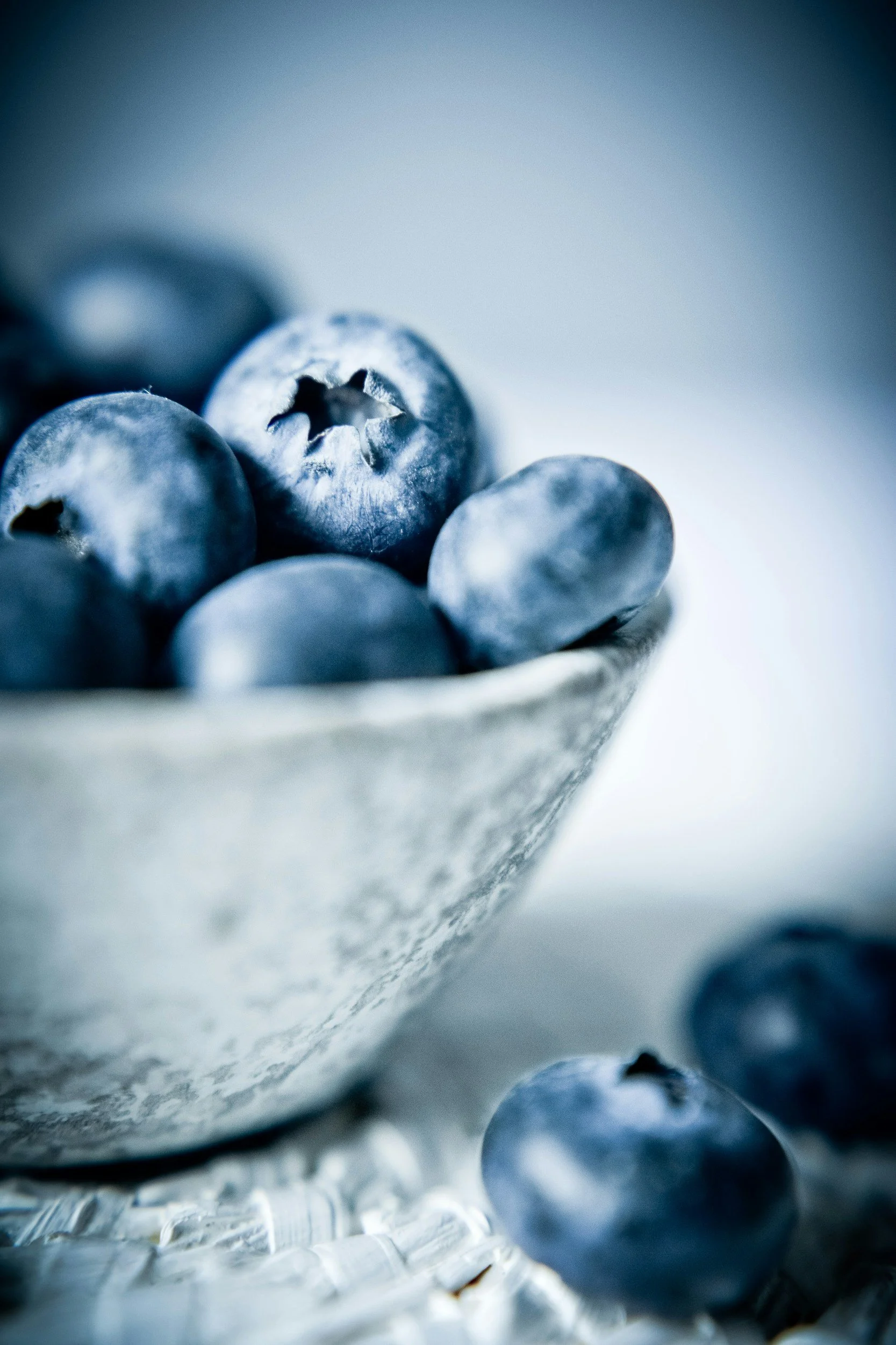 Close-up of fresh blueberries in a ceramic bowl with some blueberries scattered outside the bowl.