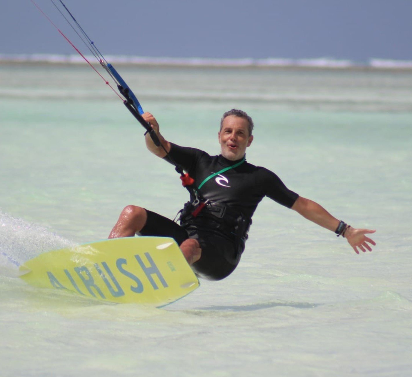 Istruttore e bike che fa kite surfing sulla spiaggia con il mare poco mosso e cielo nuvoloso sullo sfondo.