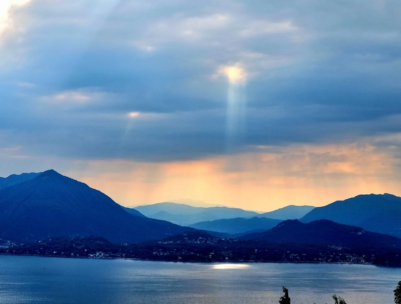 Paesaggio con montagne e un lago, cielo nuvoloso con un raggio di sole che penetra tra le nuvole.