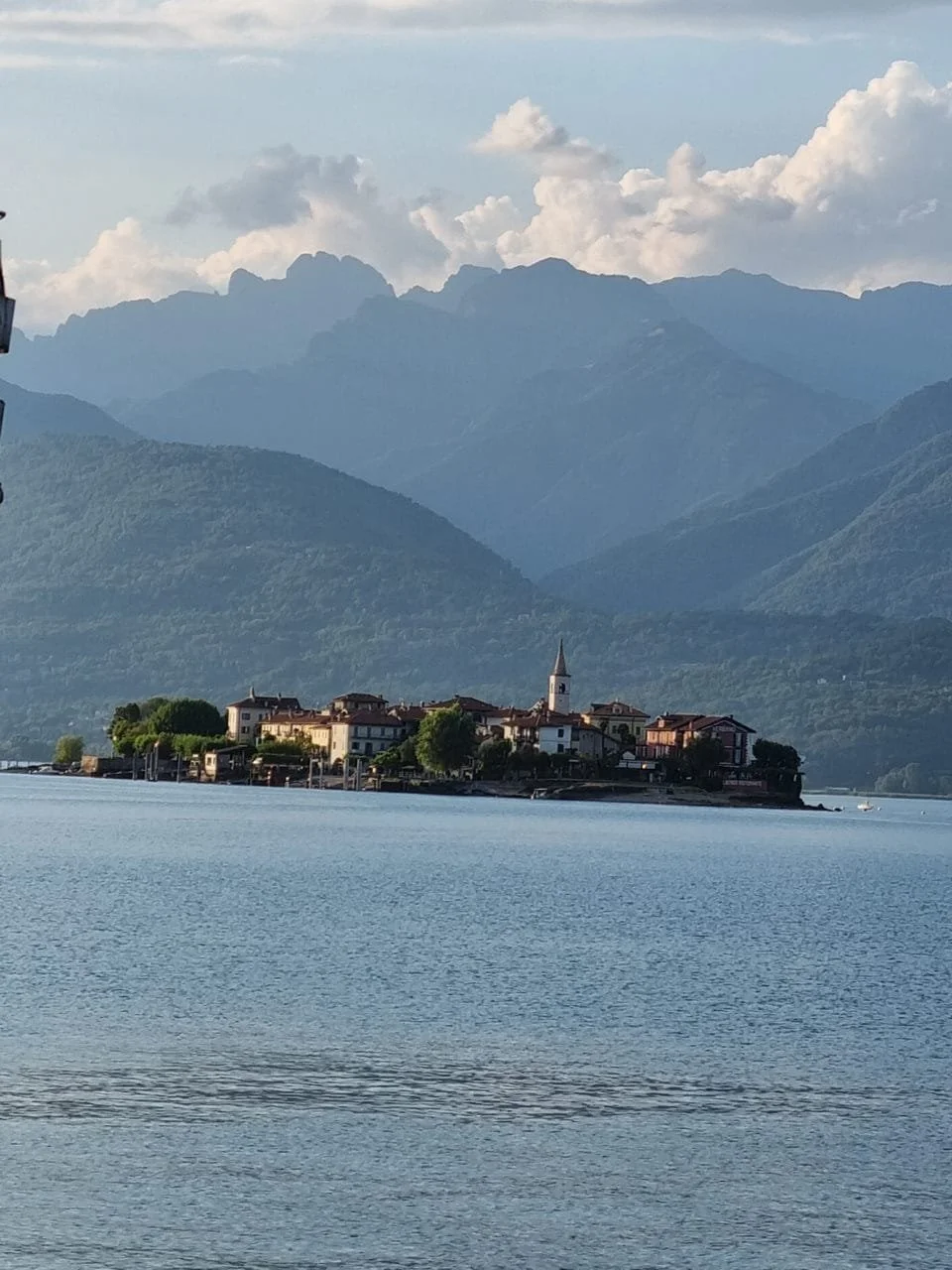 Un paesino con chiesa e case vicino a un lago con montagne sullo sfondo. Tanta natura, cielo con nuvole
