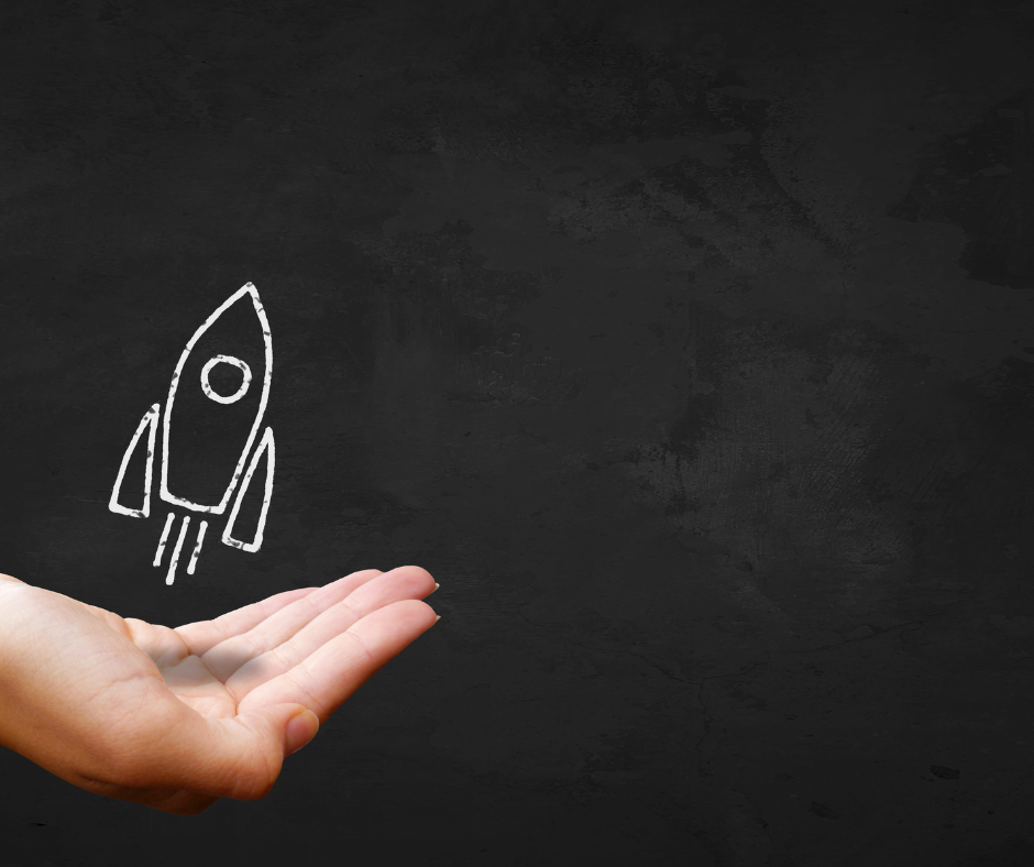 Hand holding chalk-drawn rocket ship on blackboard