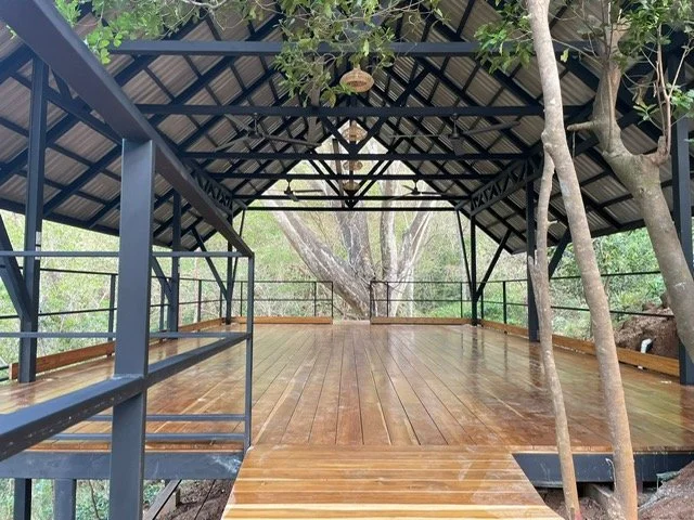 Wooden deck with a metal railing inside a gazebo surrounded by trees.