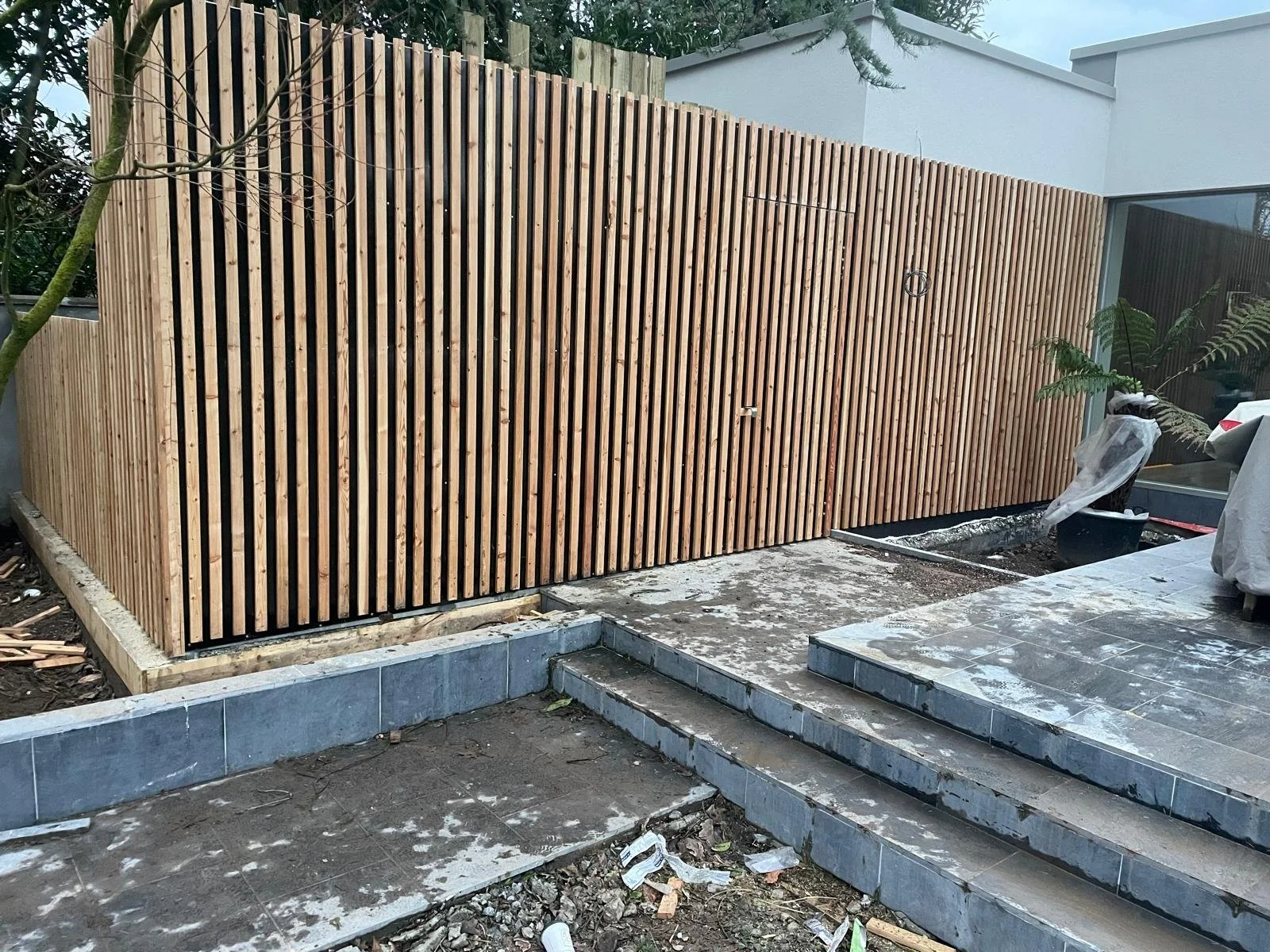 Wooden slat fence and a partially constructed outdoor patio area with steps and potted plants.