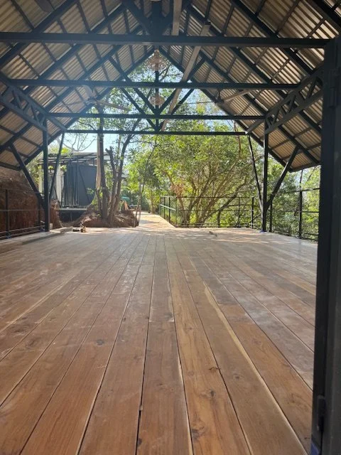 Open wooden platform or deck with a metal roof and trees visible in the background.