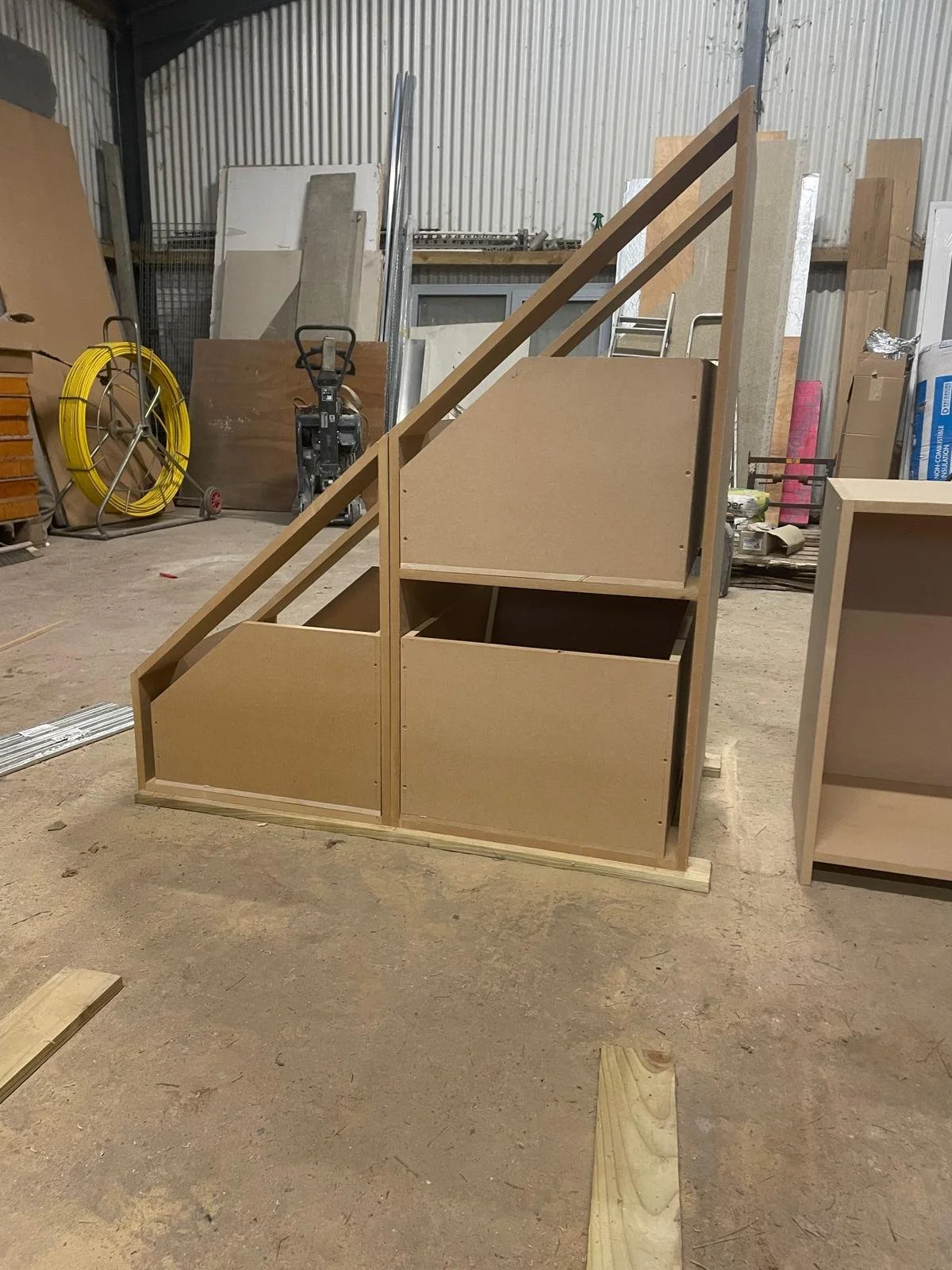 Wooden staircase structure in a workshop, with shelves and tools in the background.