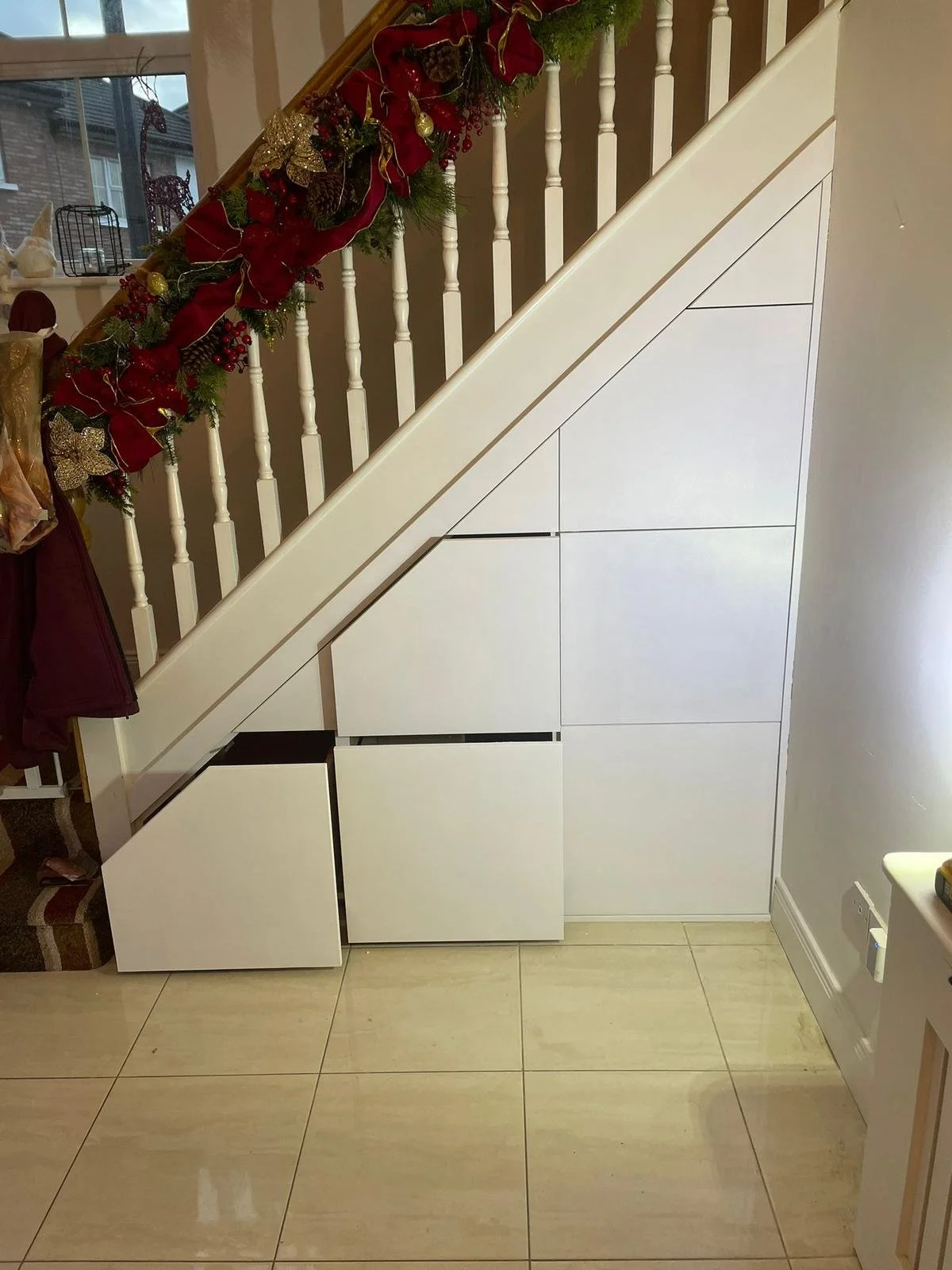 Understairs storage with white cabinets and holiday garland on the staircase railing.