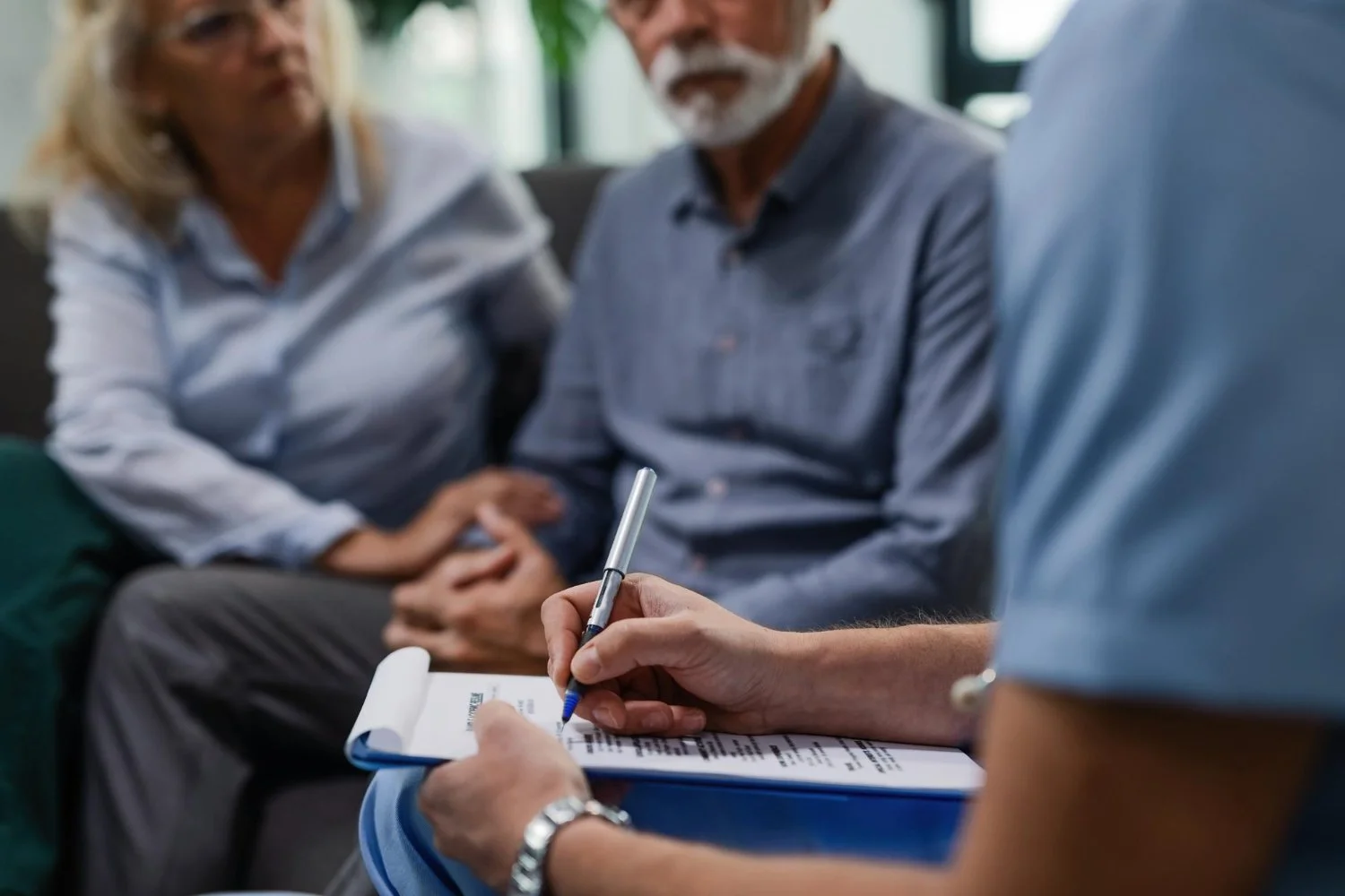 A couple sitting on a couch during a counseling session with a therapist taking notes.
