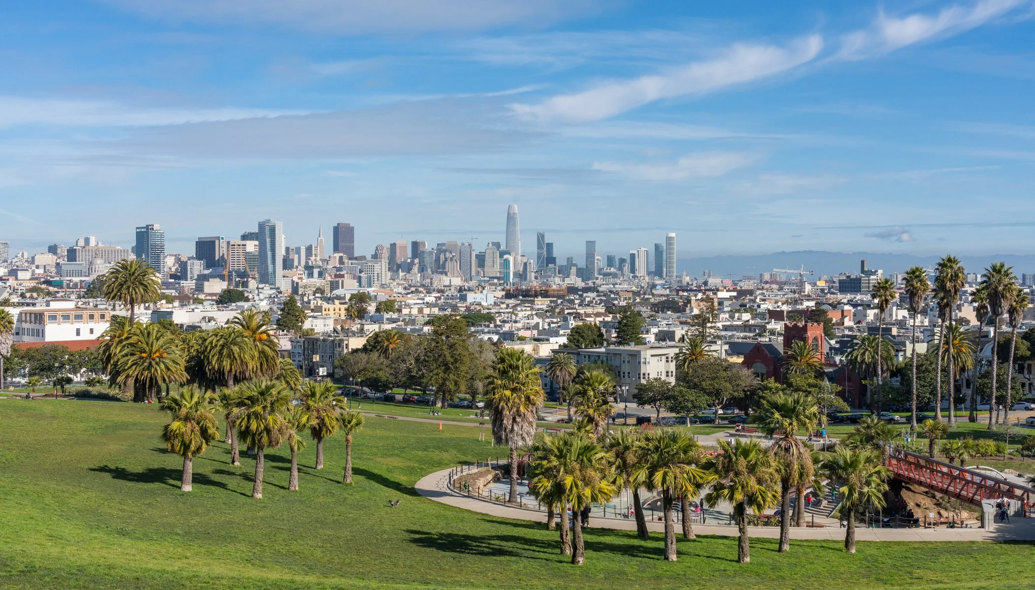 A city skyline with tall buildings in the distance and a park with palm trees in the foreground.